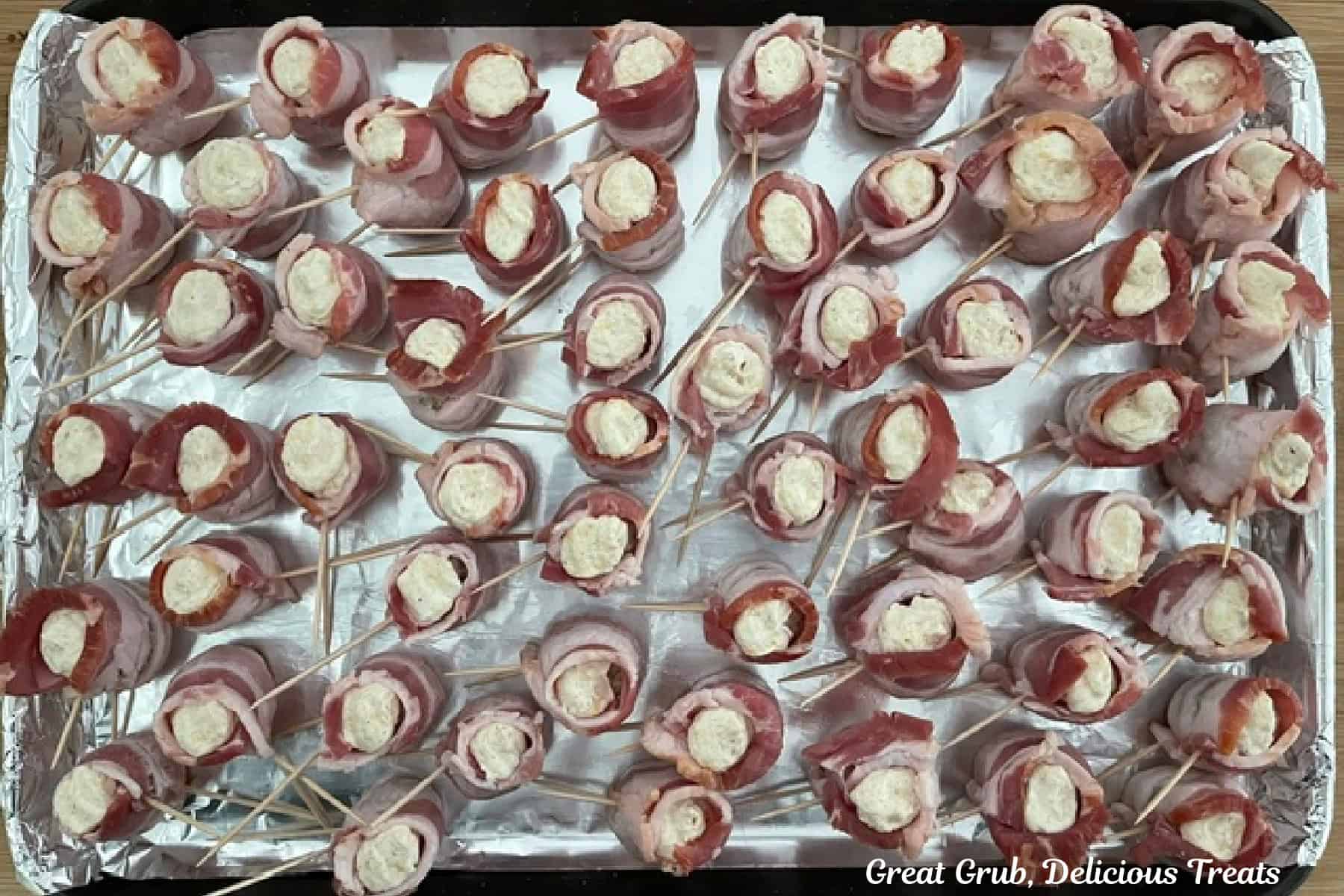 A foil lined baking sheet with meatball pig shots on it with the cream cheese filling inside the bacon "cup" like opening on top.