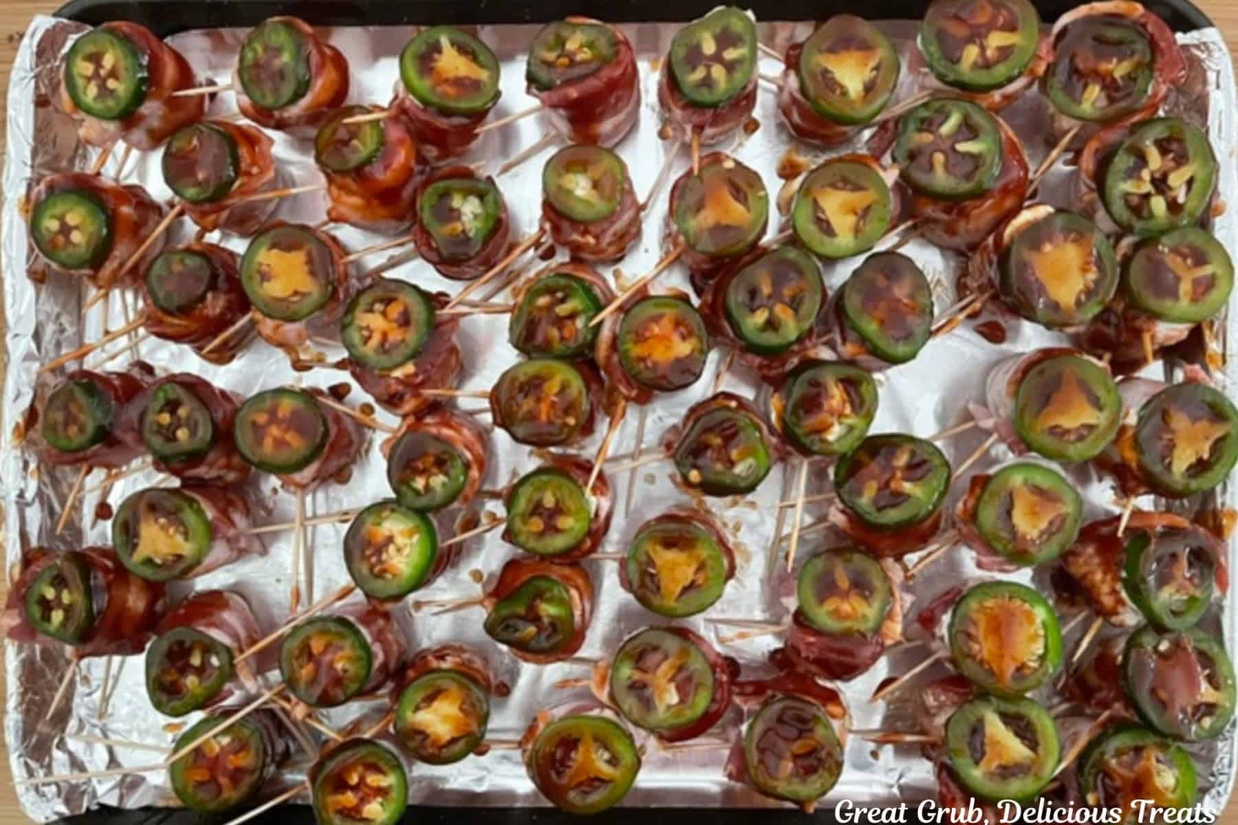 Bacon wrapped meatball pig shots on a foil lined baking sheet with a slice of jalapeno on each one, and brushed with a BBQ mixture.