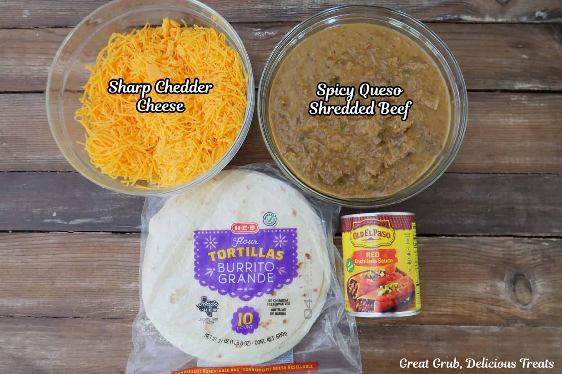 A wood surface with shredded cheese, queso shredded beef, flour tortillas, and red enchilada sauce placed on it.