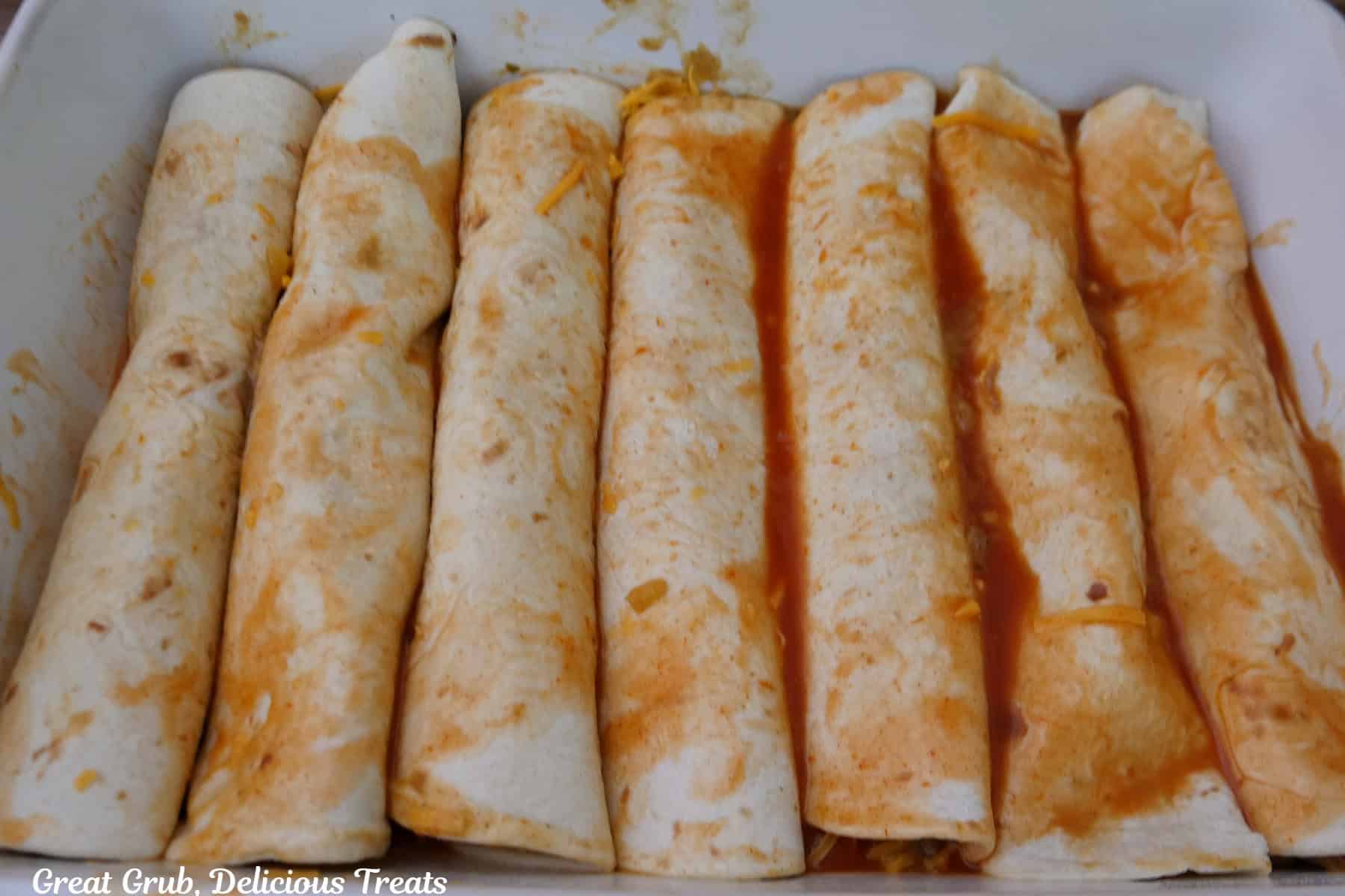 A white baking dish with seven shredded beef enchiladas placed in it after being rolled up.