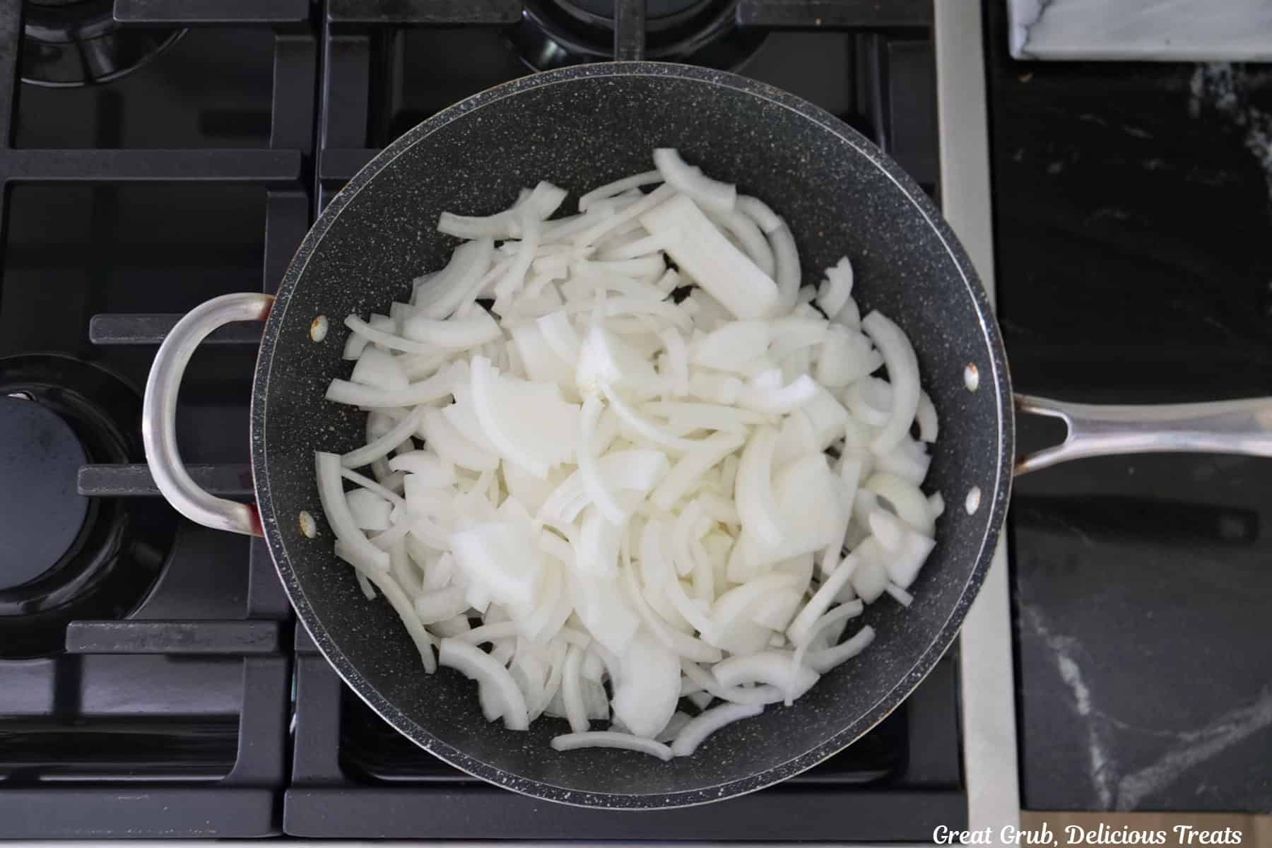 A frying pan on a stovetop with sliced white onions in it.