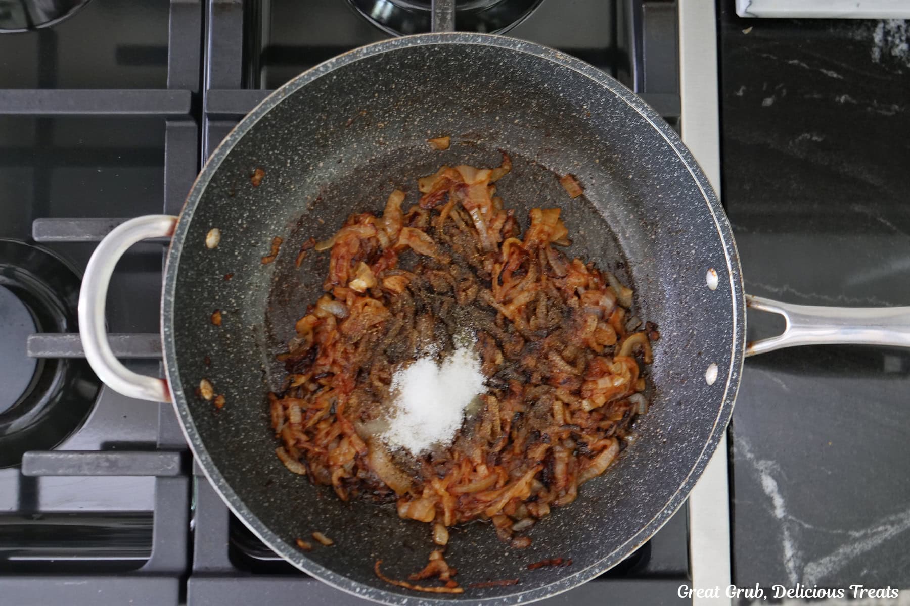 A frying pan of a stovetop with caramelized onions in it with sugar added..