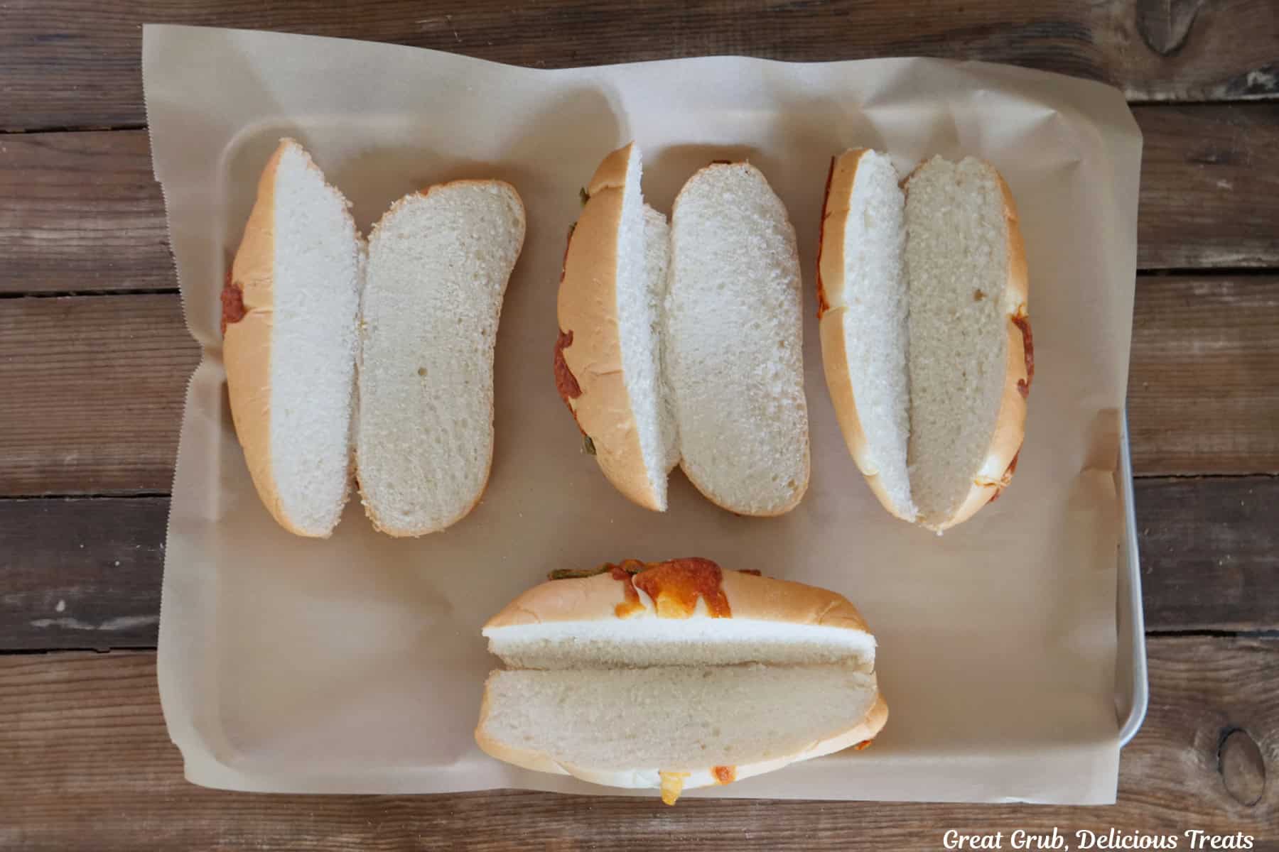 A parchment lined baking sheet with four jalapeno cheddar hoagie rolls sliced in half.