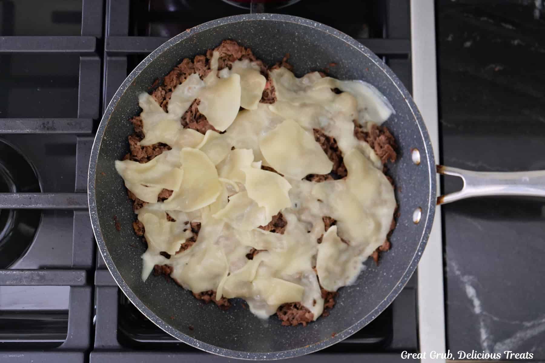 A frying pan of the stovetop with the cooked ribeye with provolone cheese placed on top of the meat.