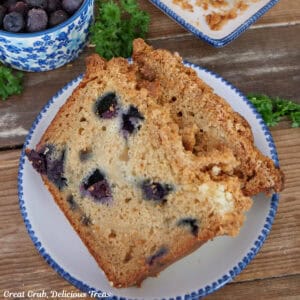A wood surface with a round white plate with two slices of blueberry cream cheese loaf on it.