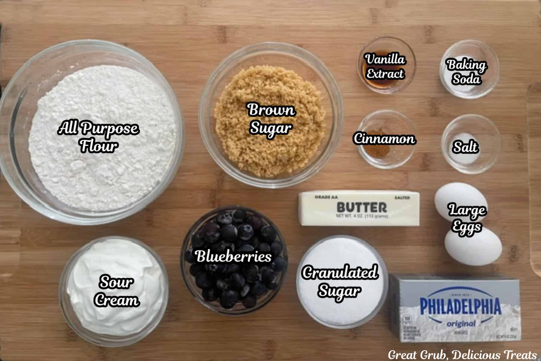 A wood surface with all the ingredients placed on it to make blueberry cream cheese loaf.
