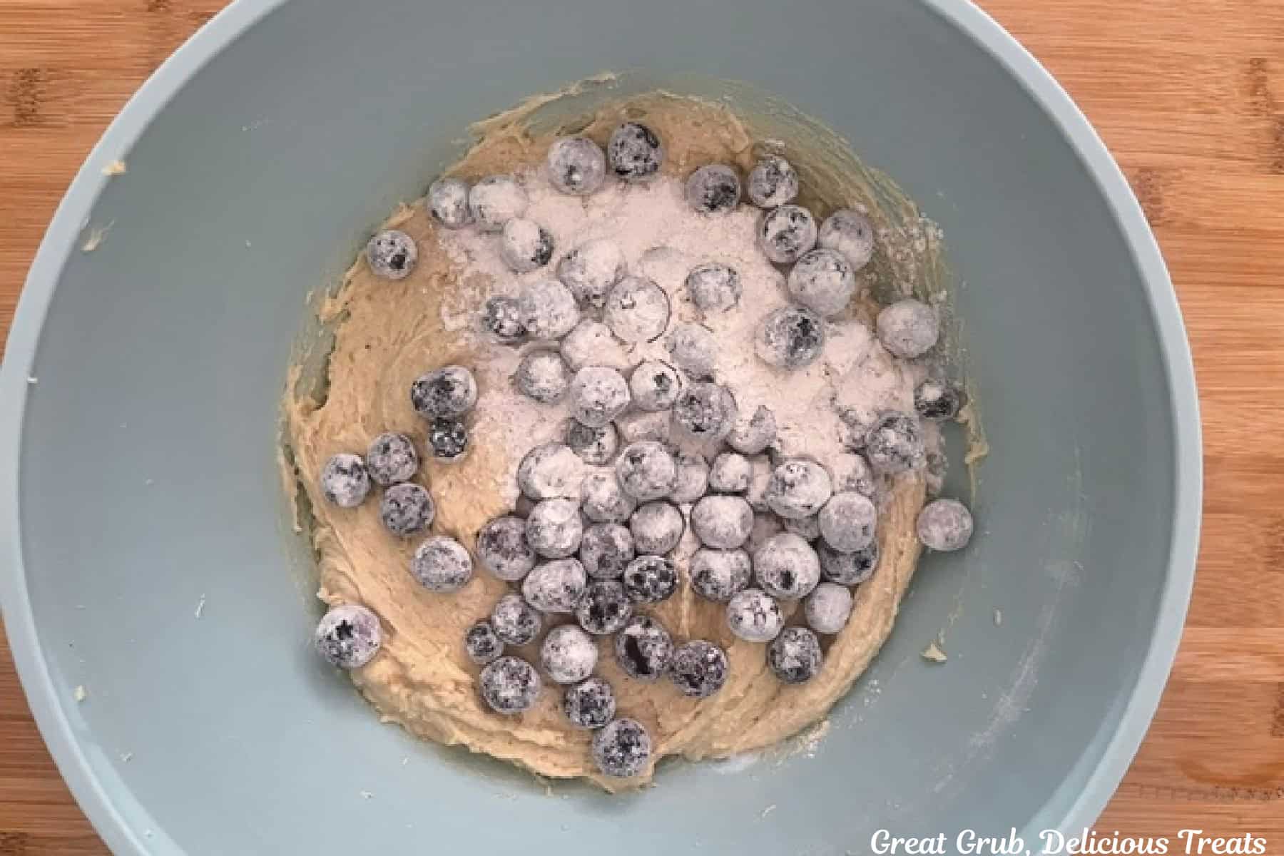 A light blue bowl with the blueberry loaf batter in it with flour coated blueberries added.