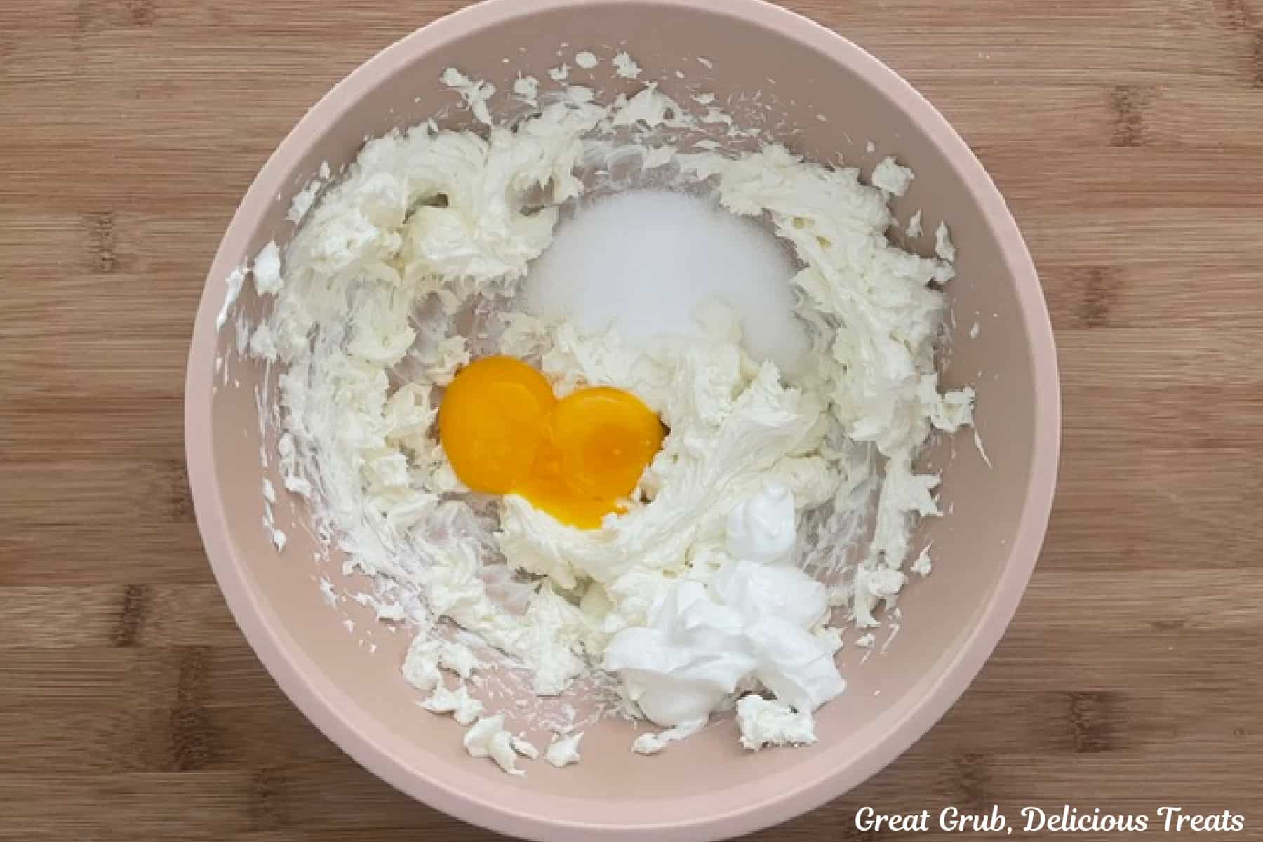 A pale pink mixing bowl with the cream cheese mixture ingredients in it before being combined.