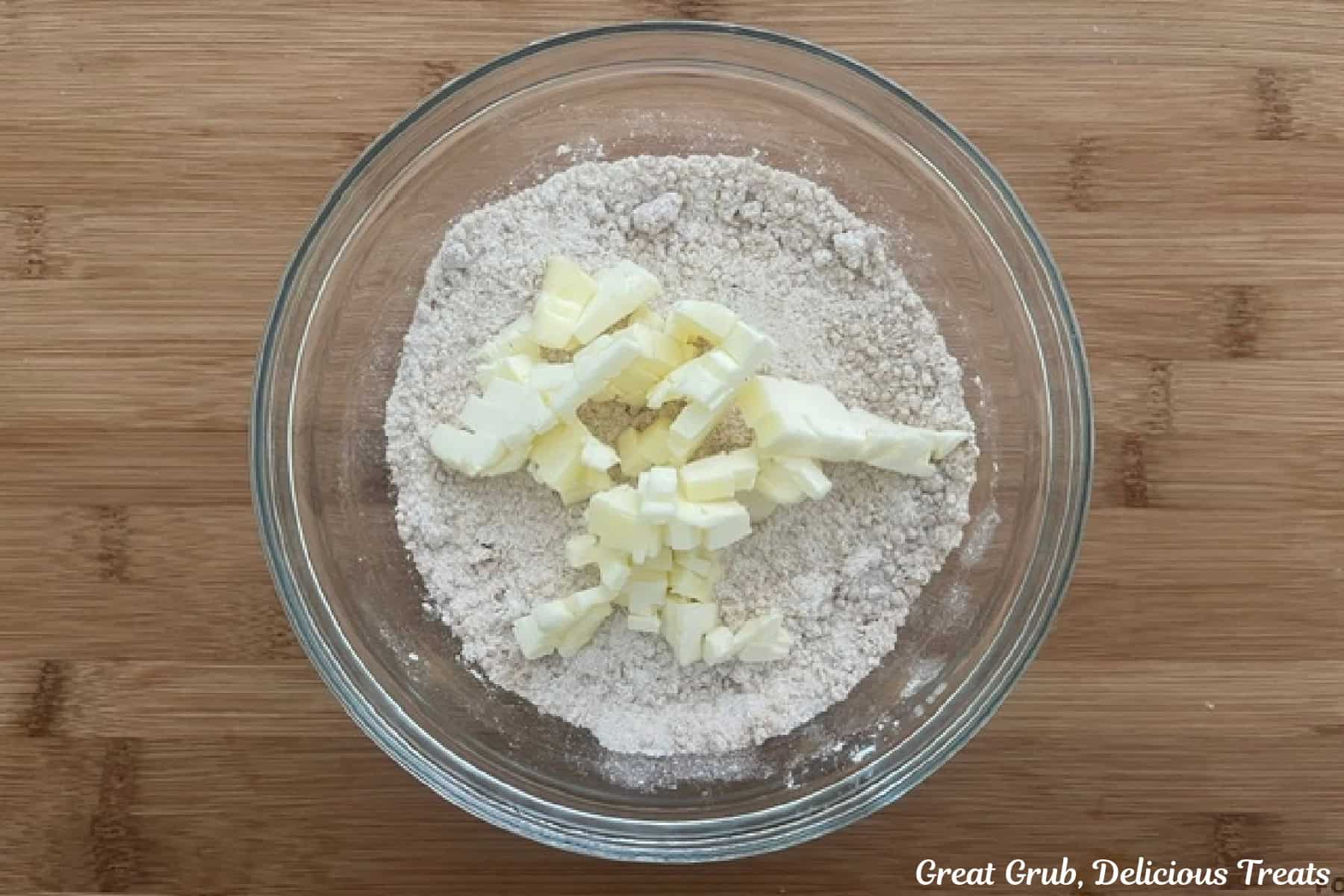 A wood surface with a glass bowl filled with the streusel ingredients in it with small cubes of butter on top before being combined.