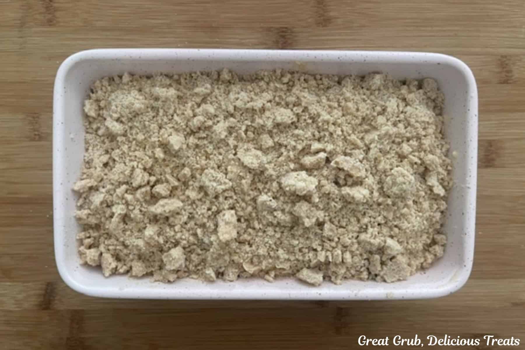 A wood surface with a with loaf pan with blueberry cream cheese loaf in it and topped with a streusel topping.