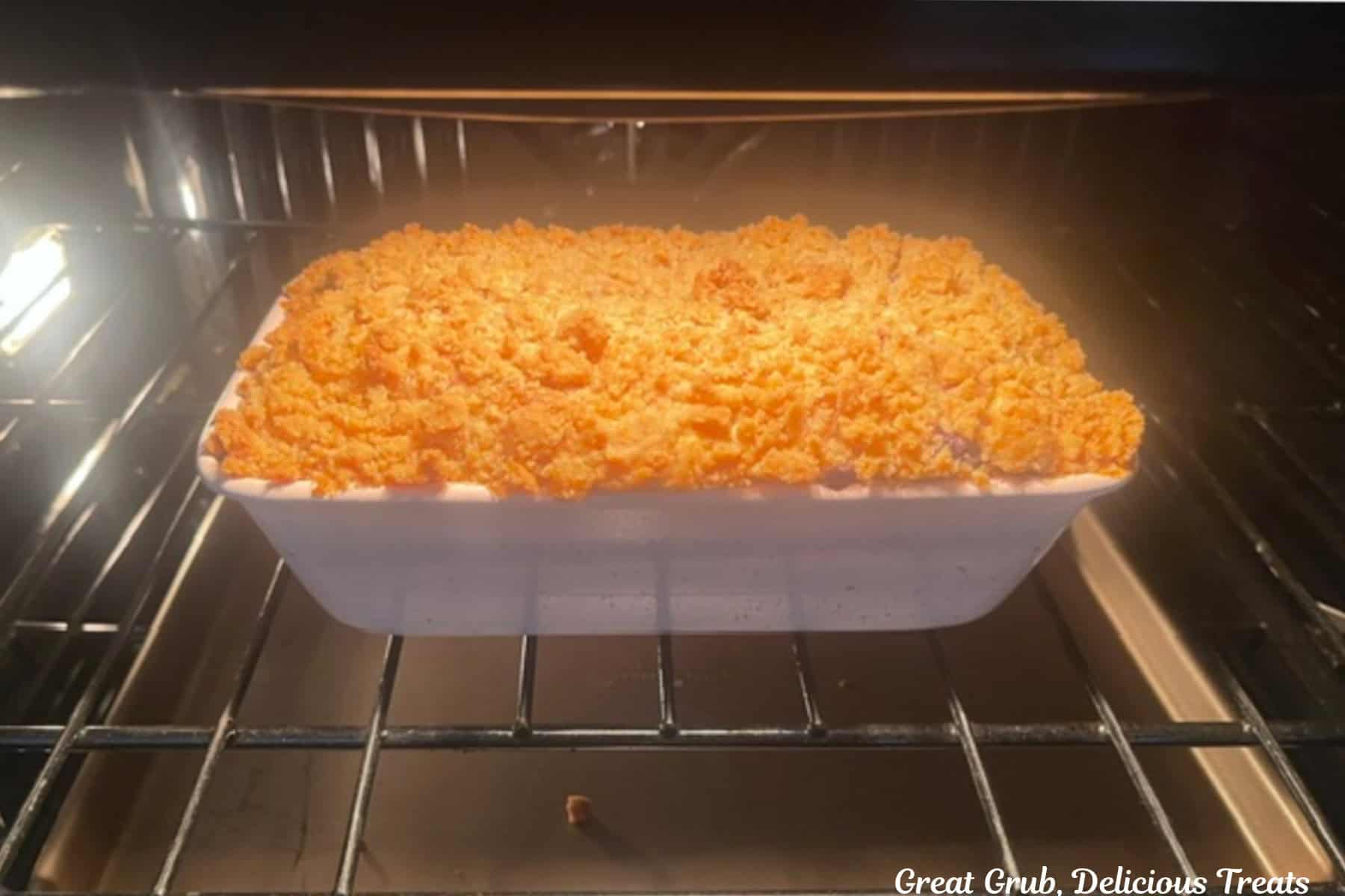An oven rack with a loaf pan filled with blueberry cream cheese filling in it being baked in the oven.