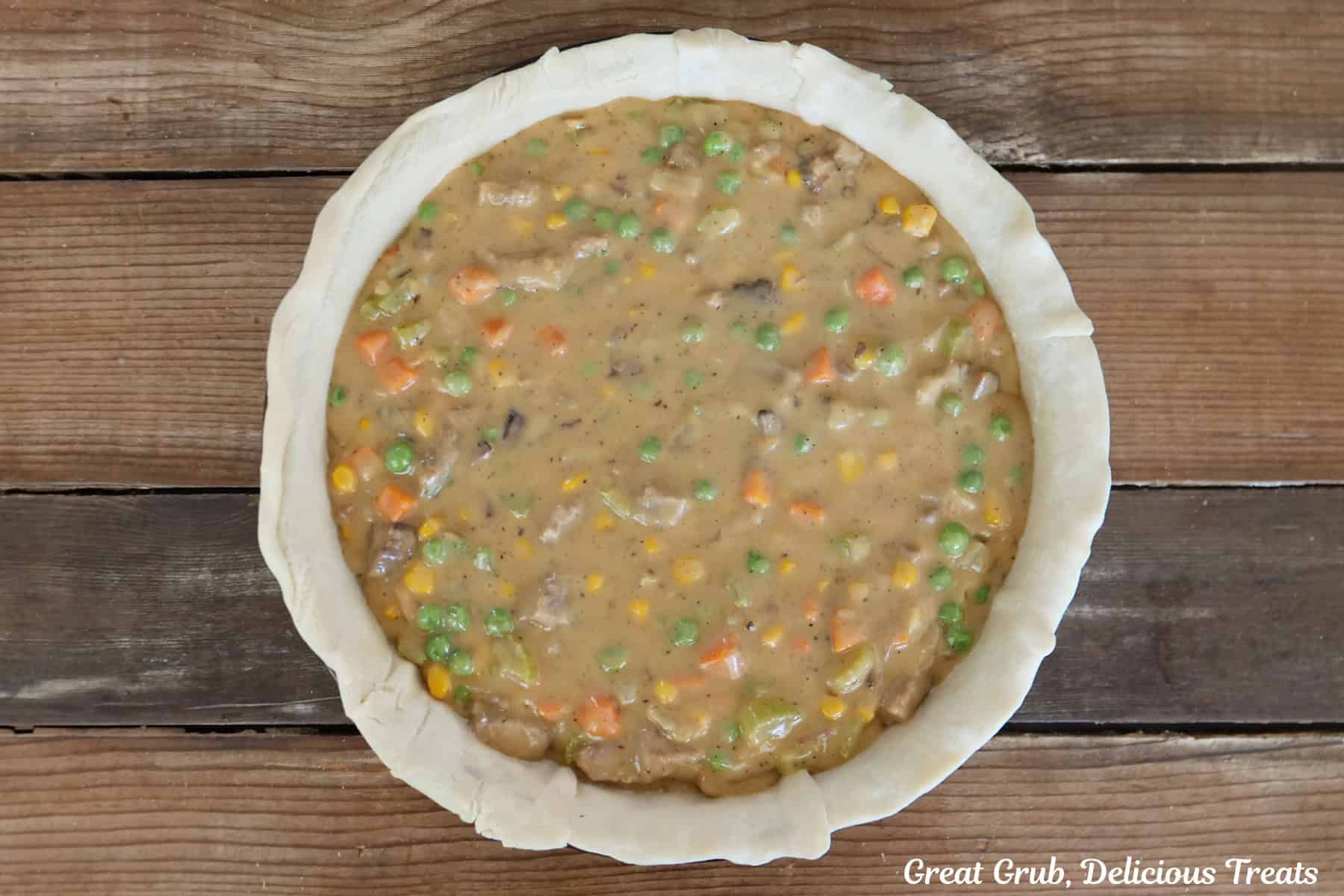 A wood surface with a pie crust filled with a rich and creamy beef brisket pot pie filling.