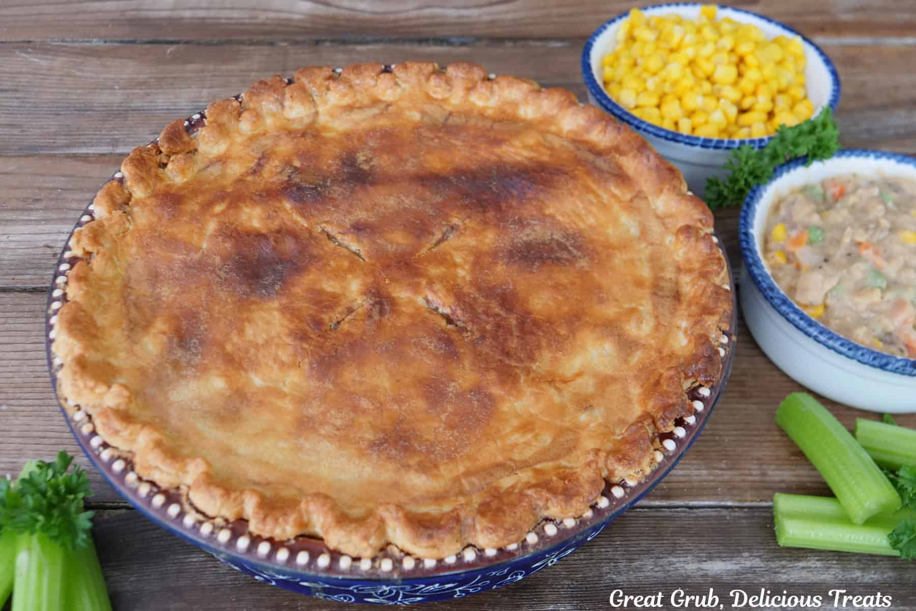 A wood surface with a golden baked pot pie on it before being sliced and served.