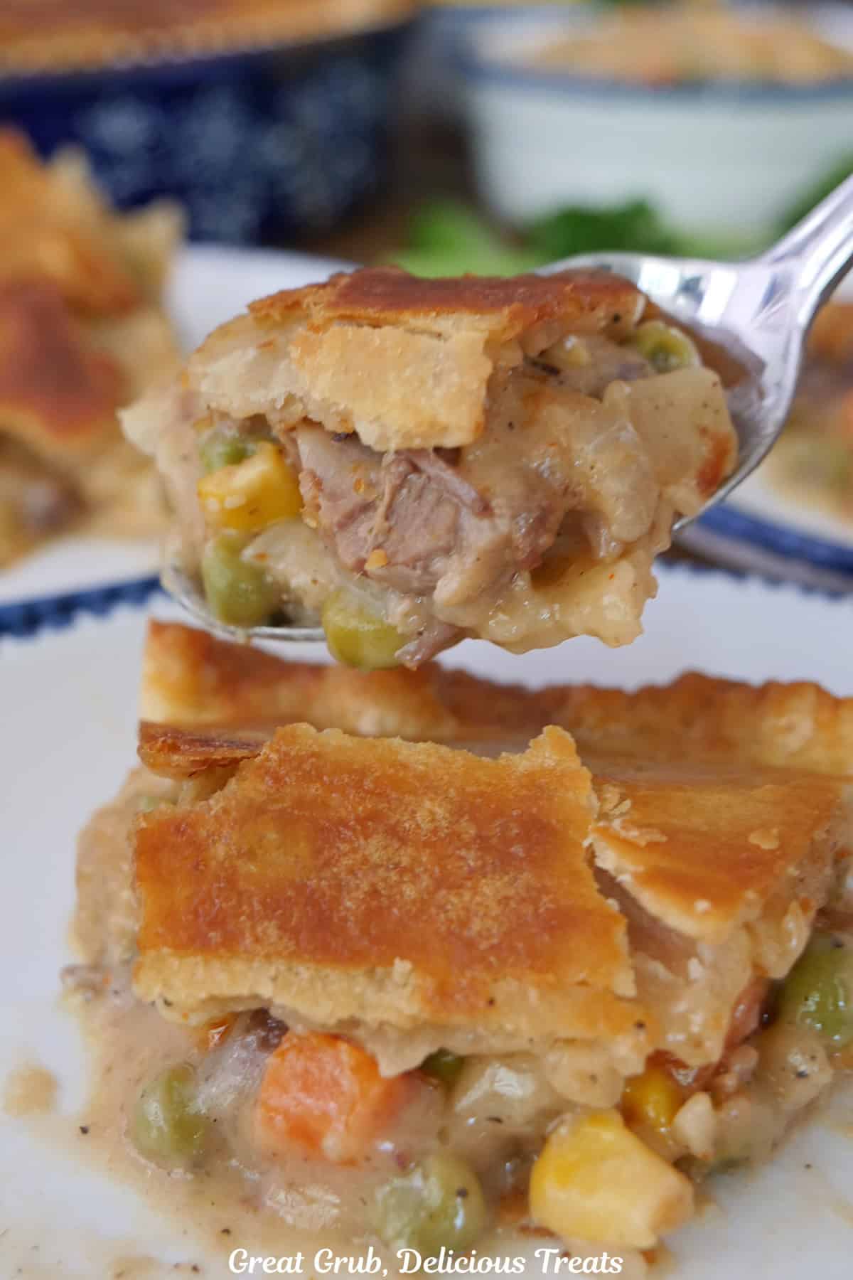 A bite of brisket pot pie on a fork with the slice below on a white plate with blue trim.