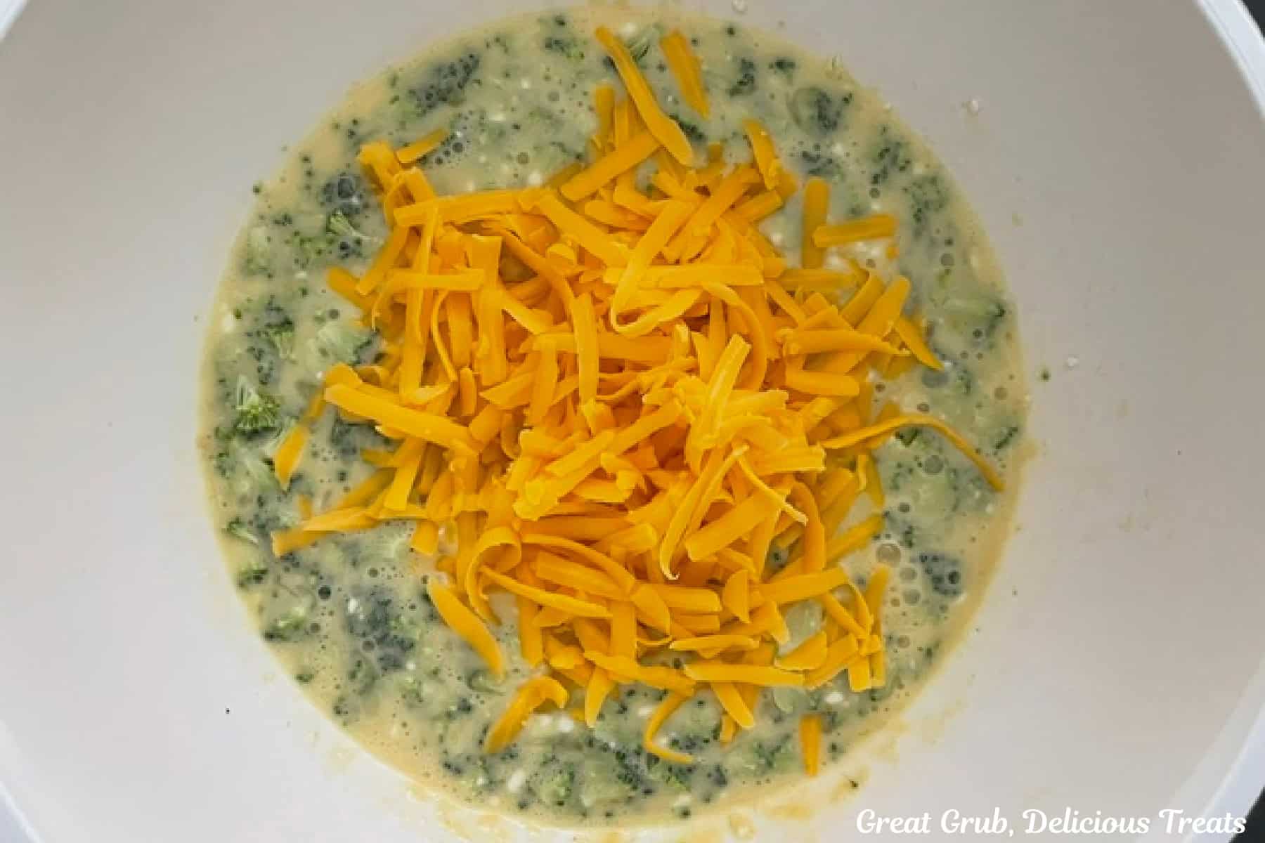 A white bowl with egg mixture mixed with broccoli and shredded cheese.