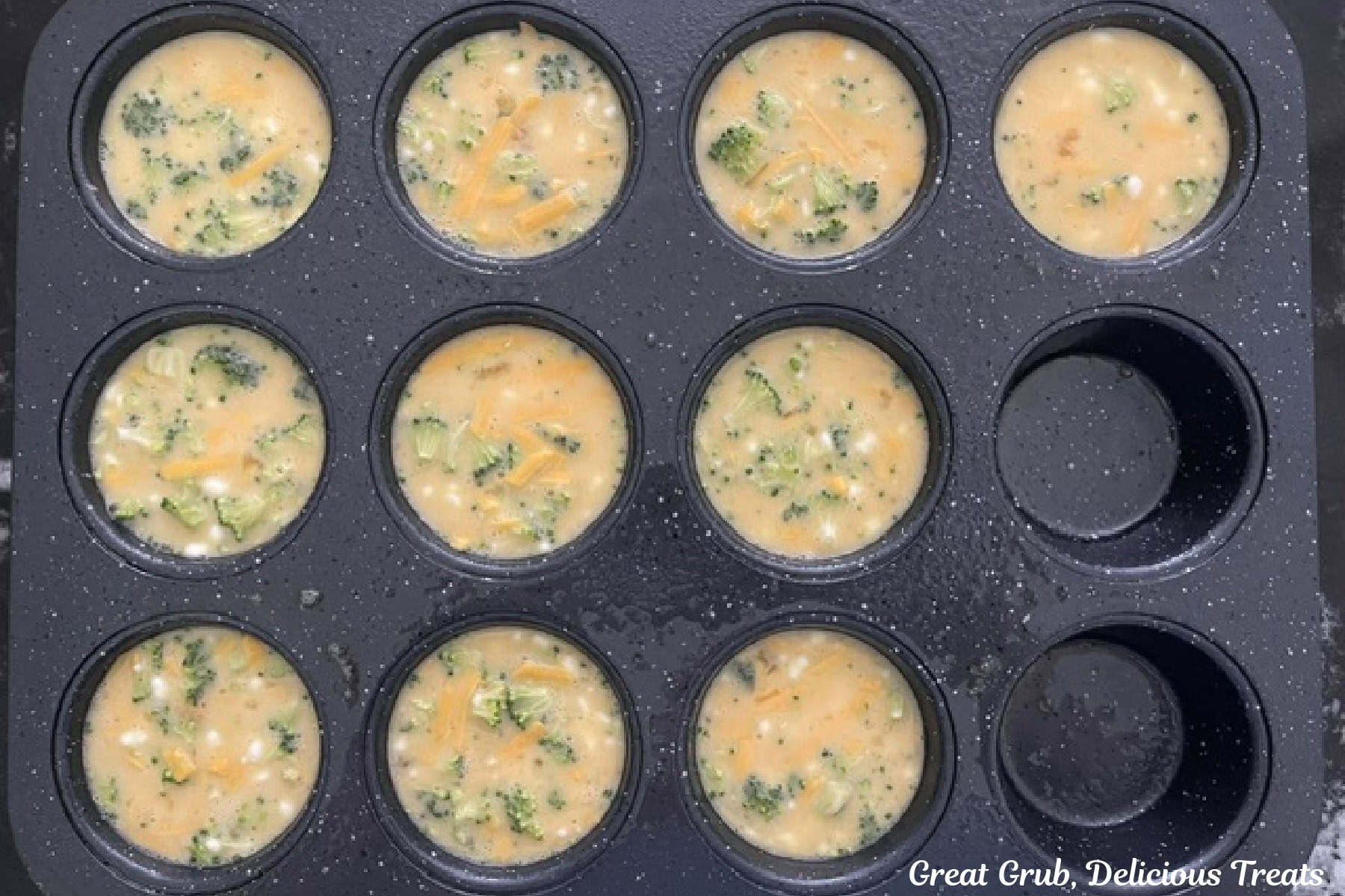 A 12-count muffin tin filled with broccoli cheddar egg mixture before being baked.