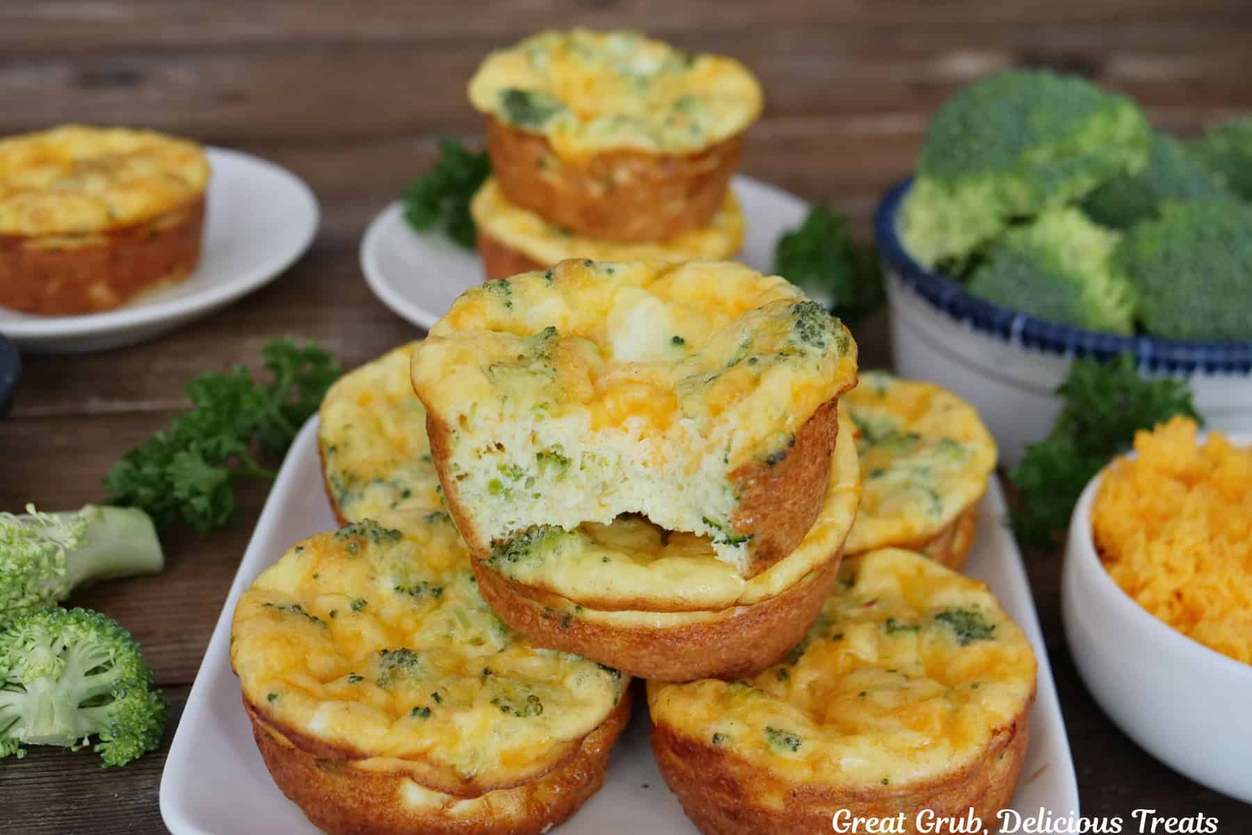 Six broccoli cheddar egg bites on a white plate with a bite taken out of the one on top.