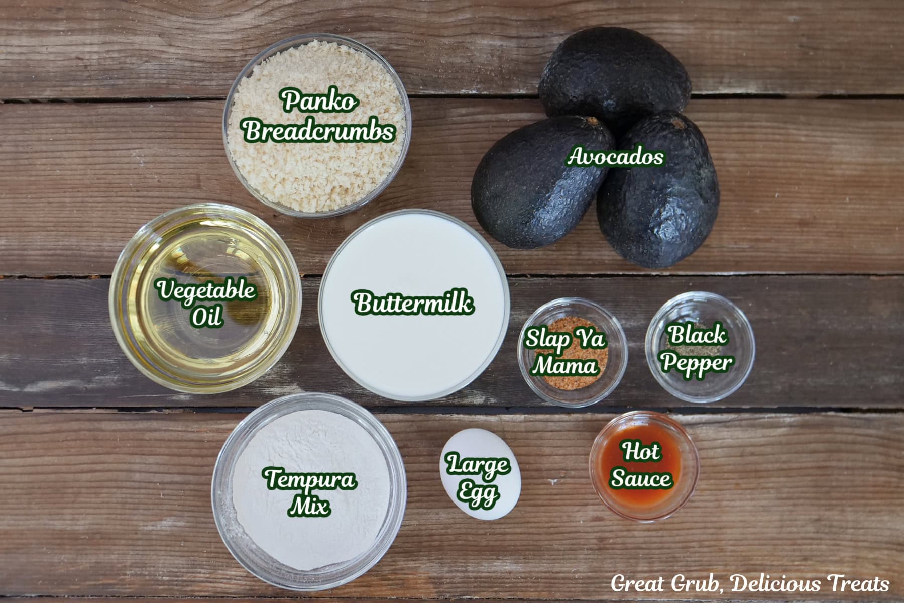 A rustic wood surface with all the ingredients placed on it to make crispy avocado fries.