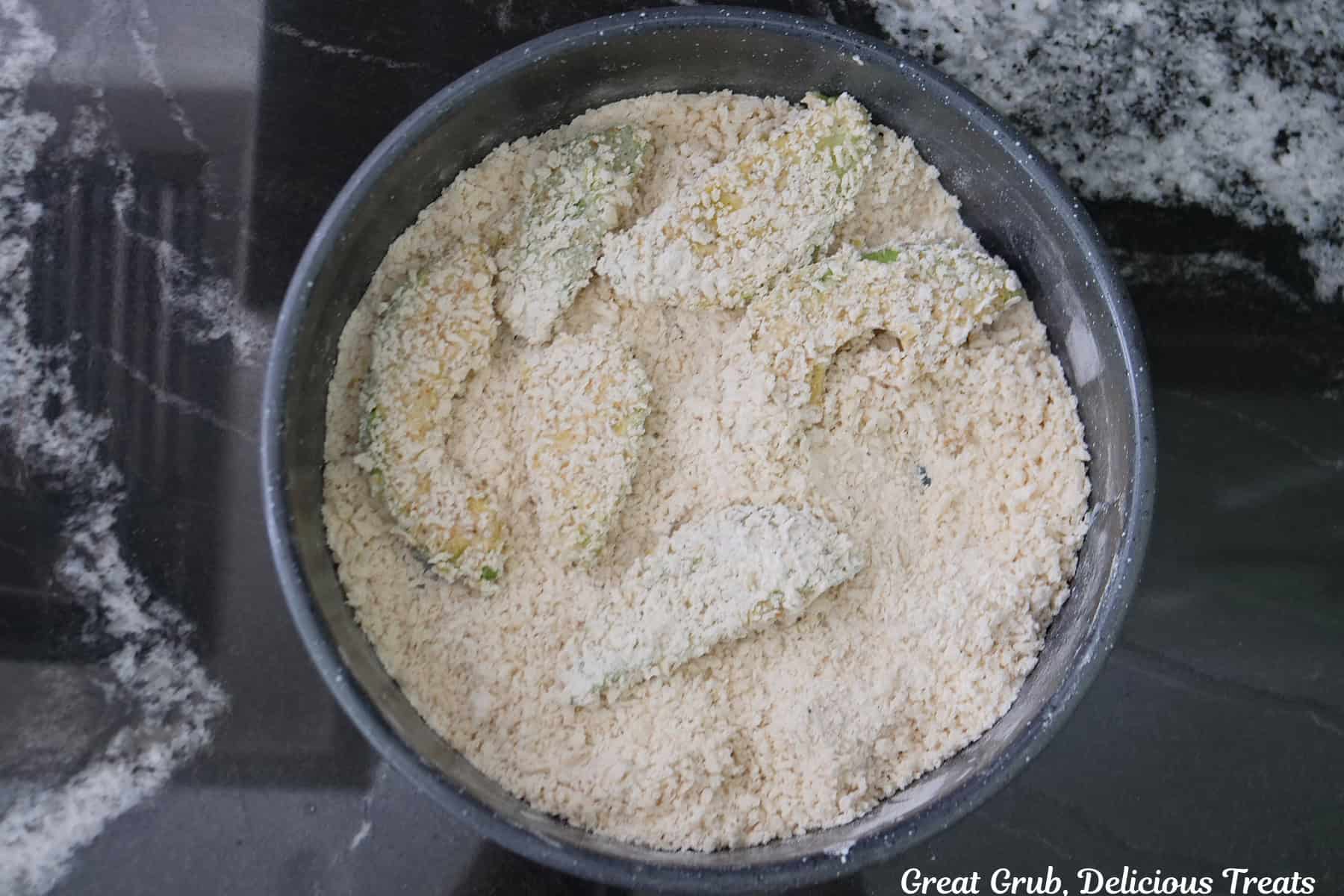 A round pan filled with seasoned breadcrumbs and a few coated avocado slices in it.