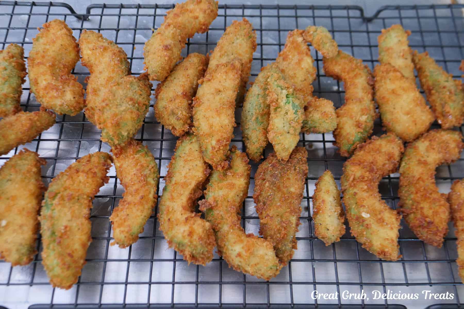 A wire rack with a couple dozen fried crispy avocado fries on it.