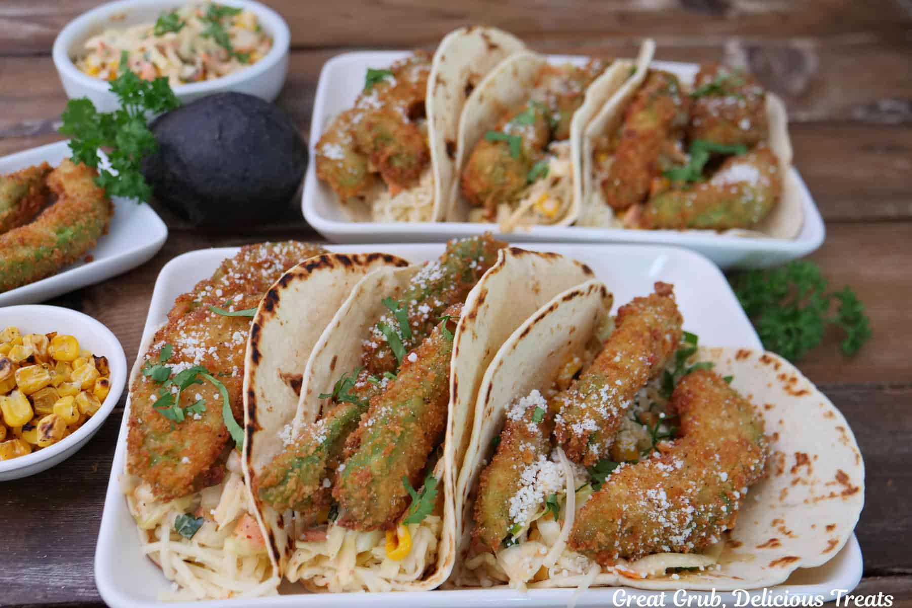 Three avocado tacos on two white oblong plates with flour tortillas and crispy fried avocado fries.