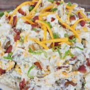 A rustic wood surface with a big bowl of loaded baked potato salad in it with a title overlay at the top.