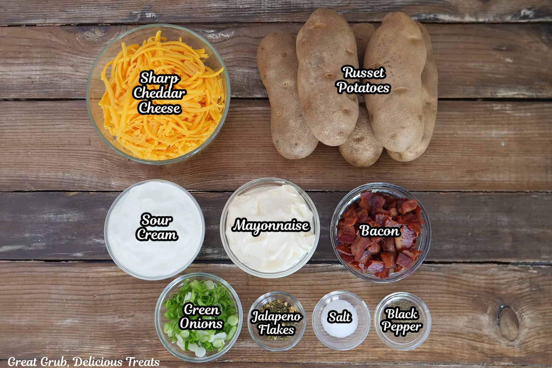 A wood surface with all the ingredients placed on it to make loaded baked potato salad.