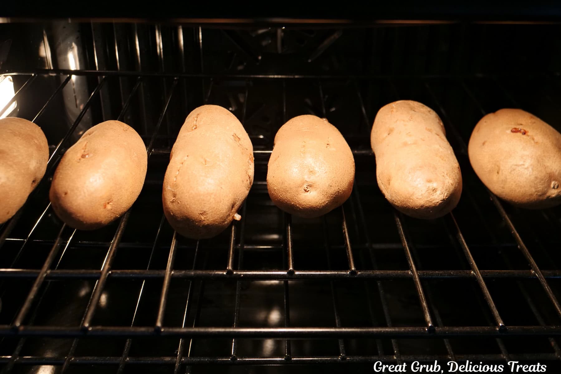 Six large russet potatoes in the oven baking on the oven rack.