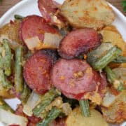 A white small round plate with a serving of Parmesan crusted smoked sausage, potatoes, and green beans on it, and a title overlay at the top.