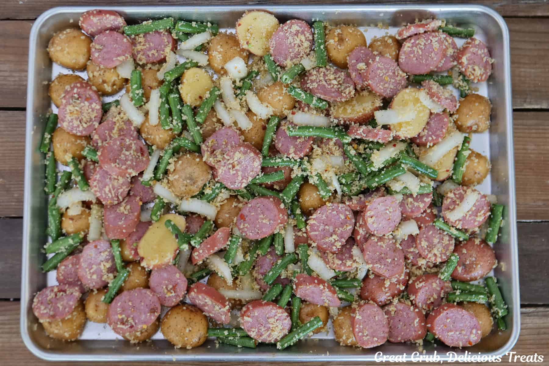 A baking sheet with all the Parmesan crusted smoked sausage and potatoes ingredients on it before being baked.