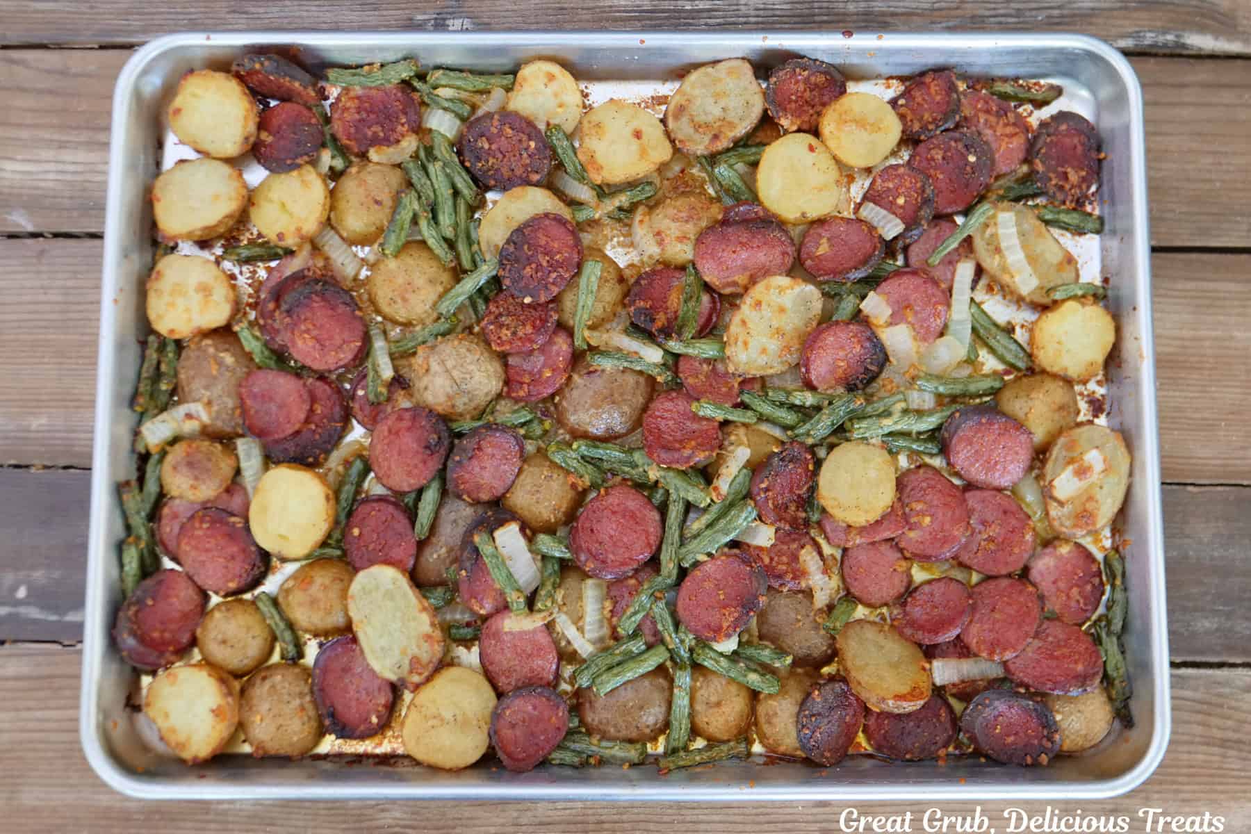 A baking sheet with all the Parmesan crusted smoked sausage and potatoes ingredients on it after being baked.