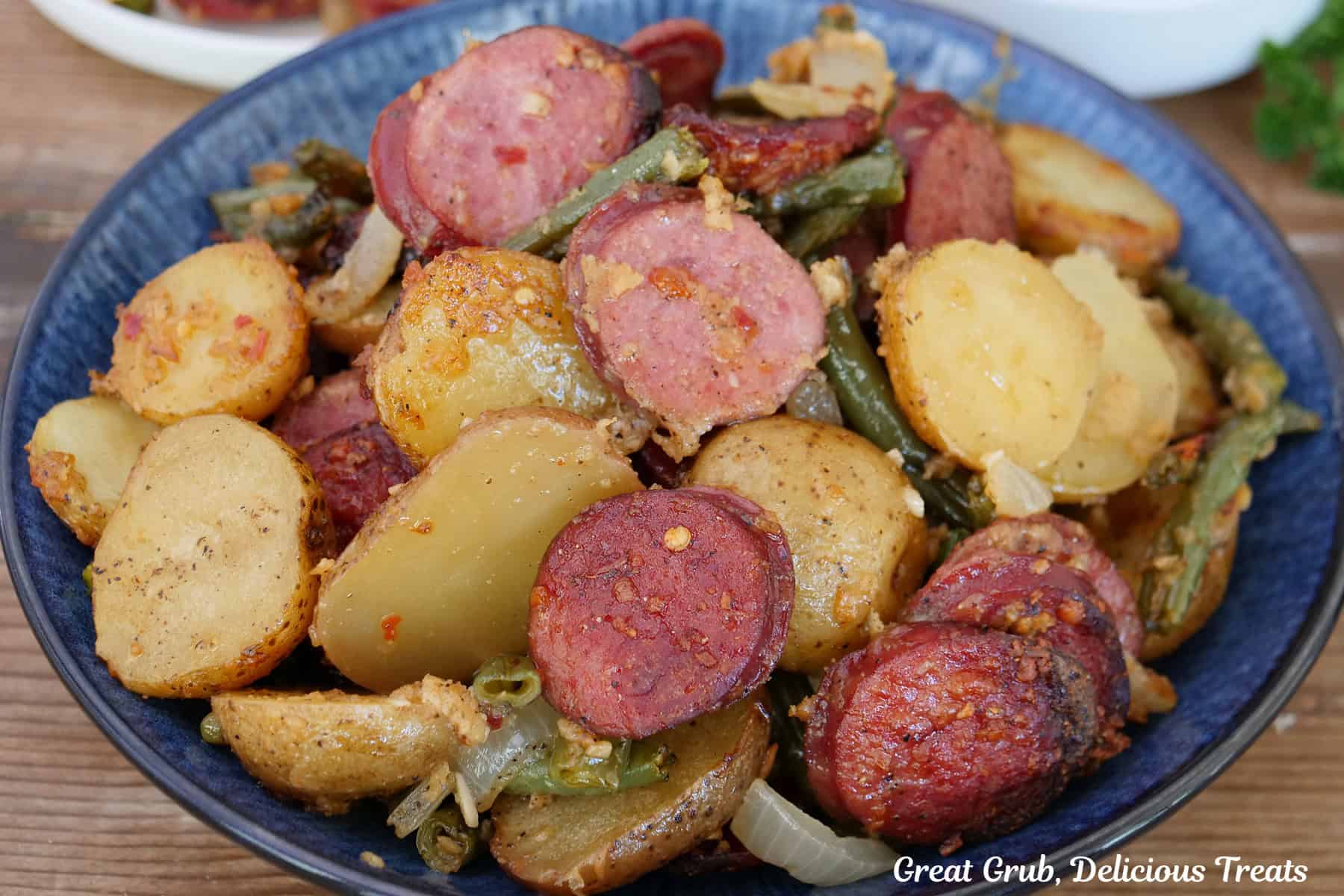 A blue bowl filled with a serving of of Parmesan crusted smoked sausage and potatoes.