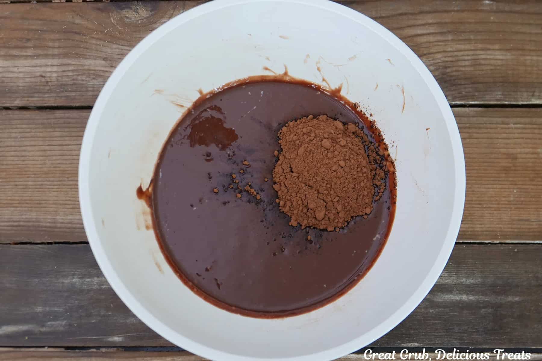 A white mixing bowl with brownie batter with cocoa powder added.