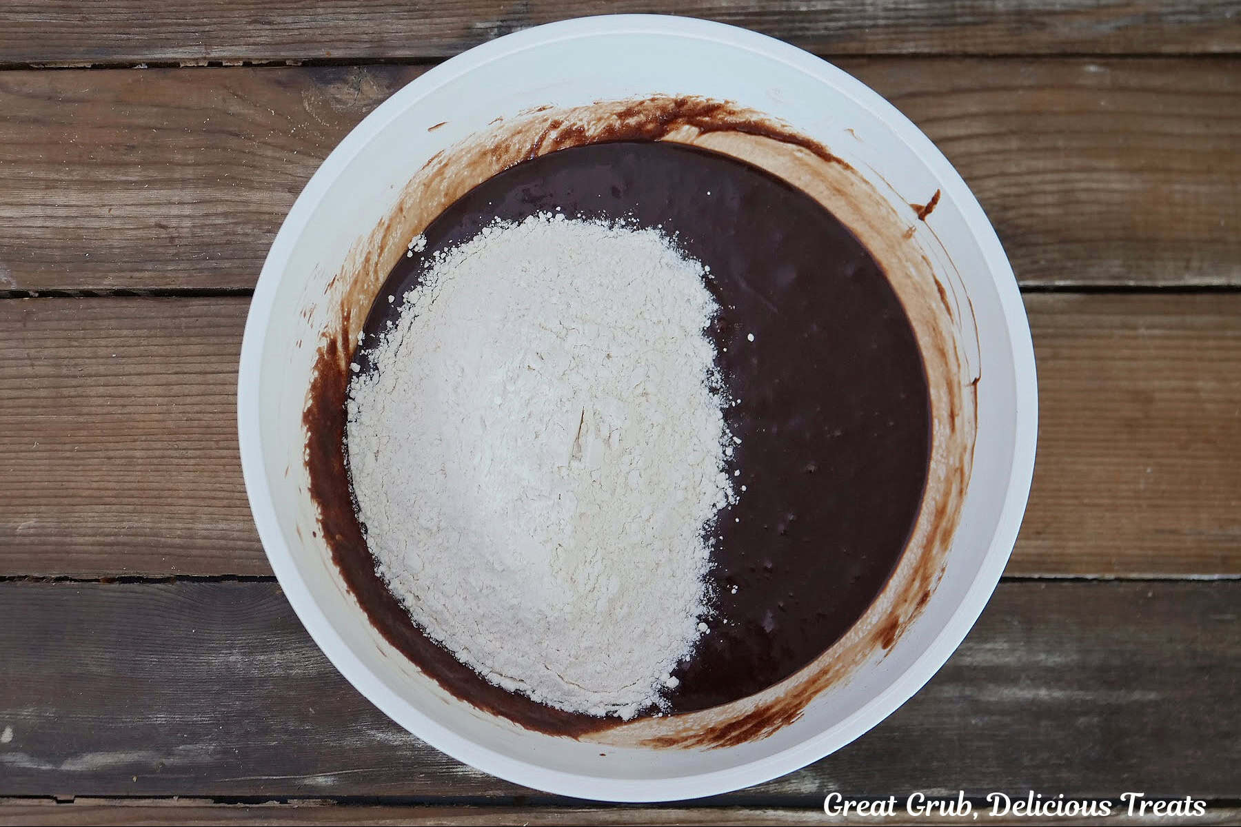 A white mixing bowl with brownie batter and flour added to it.