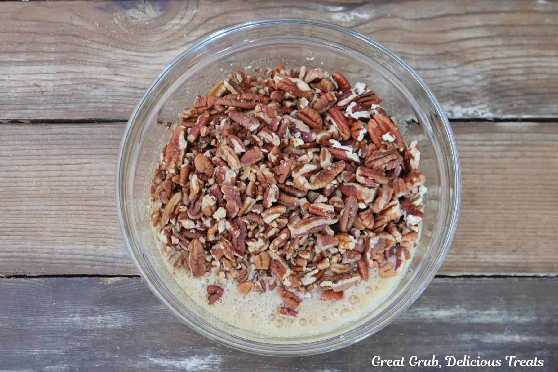 A rustic wood surface with a glass bowl filled with the pecan pie topping in it.