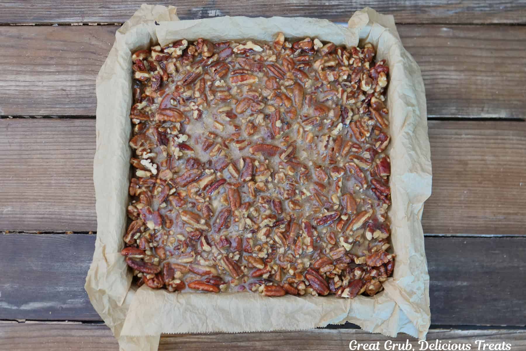 A rustic wood surface with a 9 by 9 baking dish with the brownies and pecan pie added to the top.