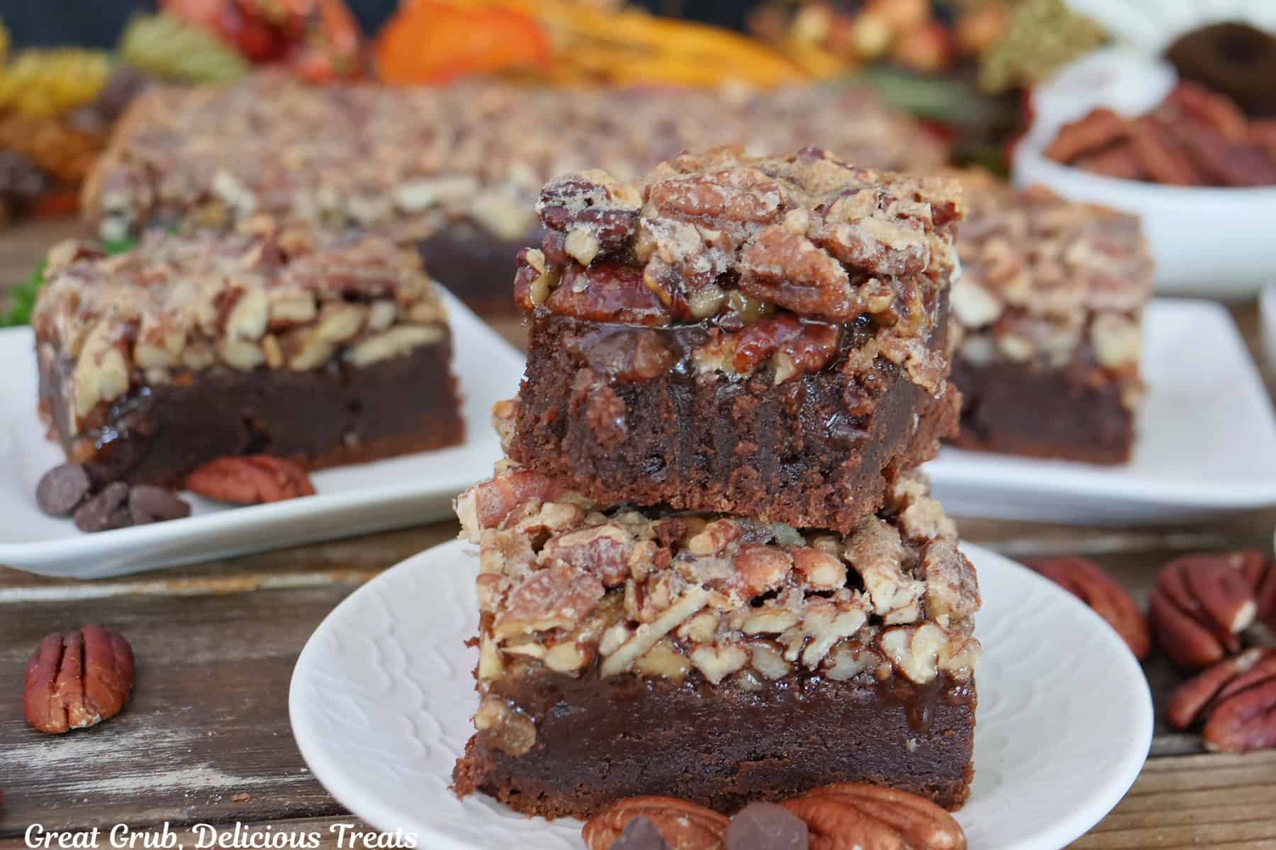 A wood surface with three white plates with pecan pie brownies on them with more brownies in the background.