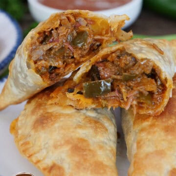 Three pulled pork empanadas on a white plate with blue trim with one cut in half showing the inside ingredients, and a title overlay at the top.