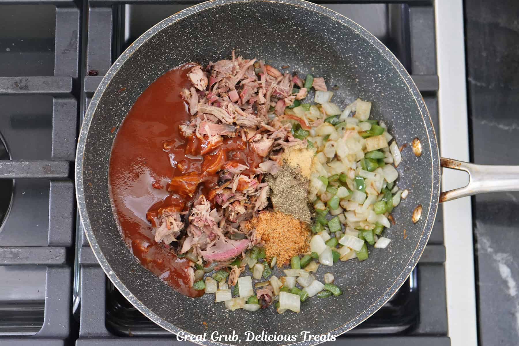 A frying pan on a stovetop with all the ingredients in it to make pulled pork empanadas.