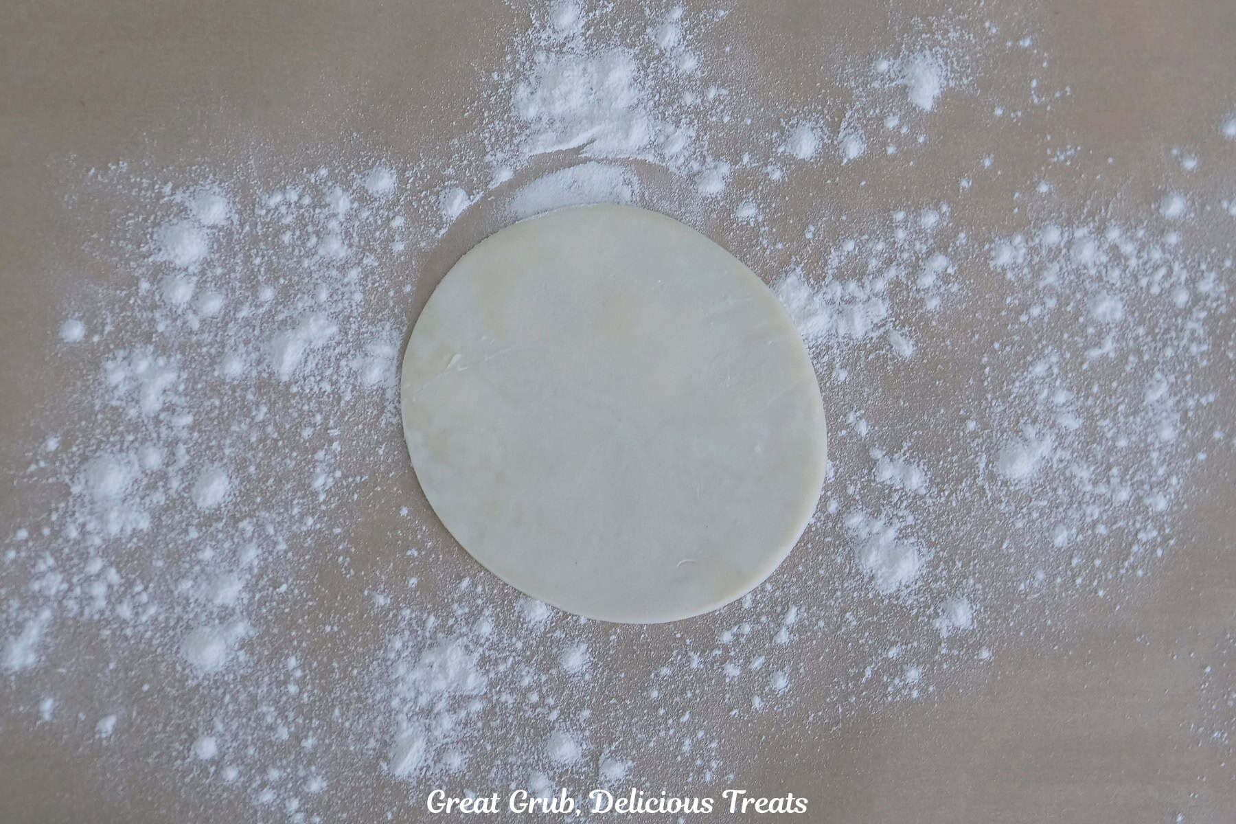 A lightly floured surface with a round empanada dough on it.