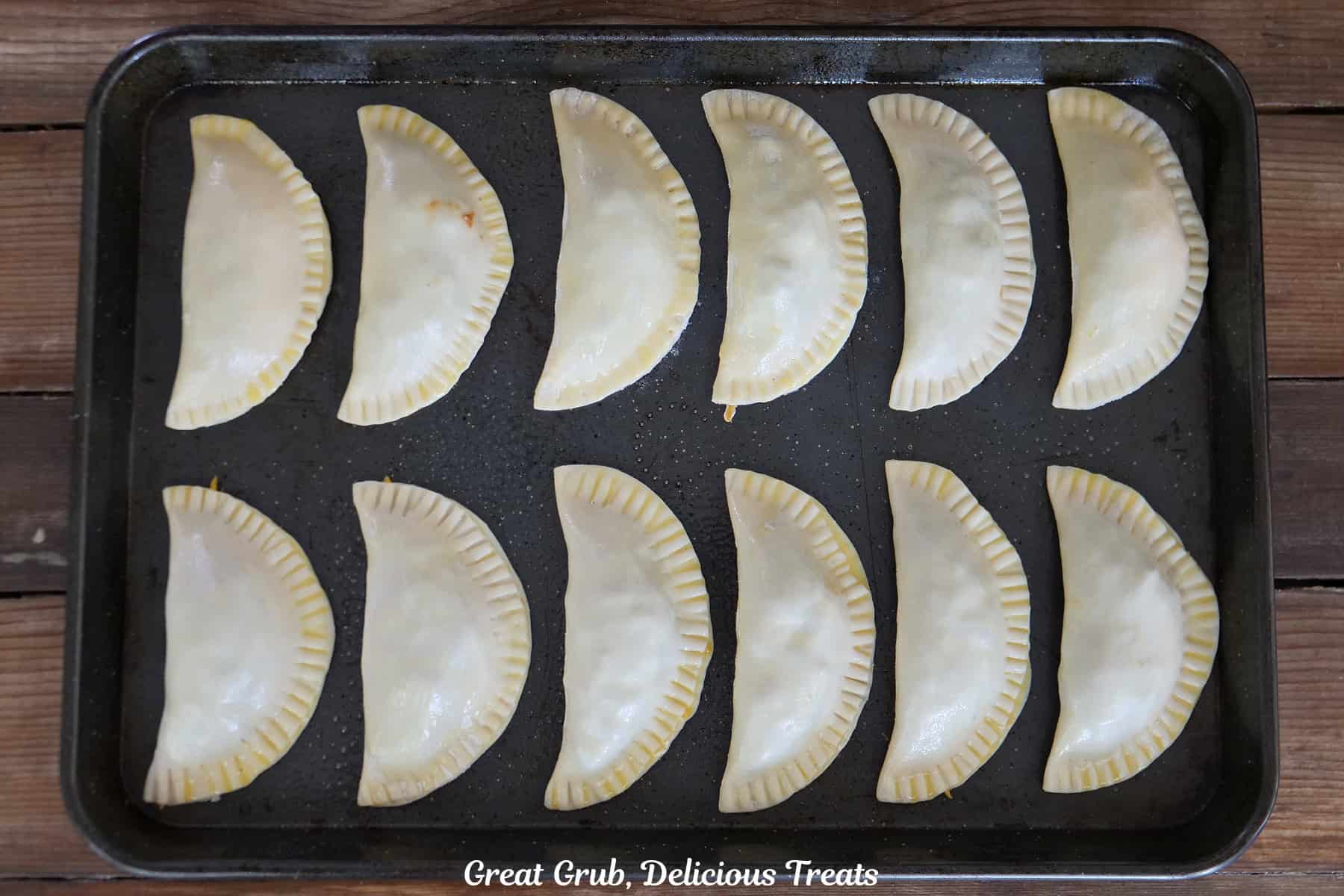 A baking sheet with twelve stuffed empanadas on it before going in the oven.