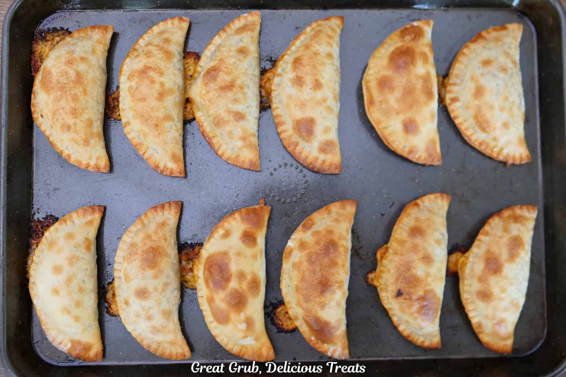 A baking sheet with twelve baked pulled pork empanadas on it.