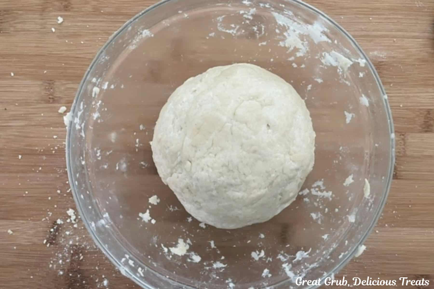 A glass bowl with a ball of pie dough in it and it's placed on a wood cutting board.