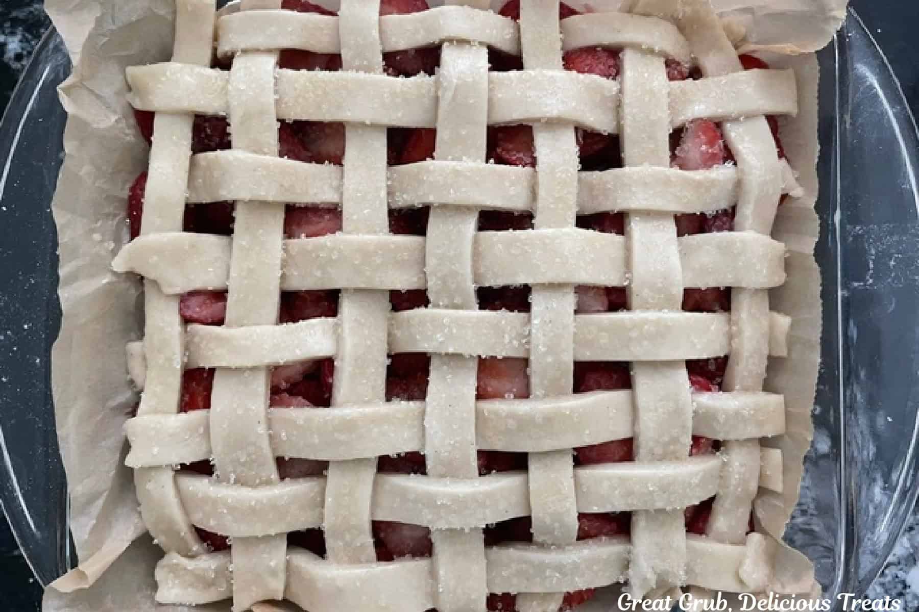 A glass baking dish with a lattice homemade pie crust placed on top of a fresh strawberry pie filling.