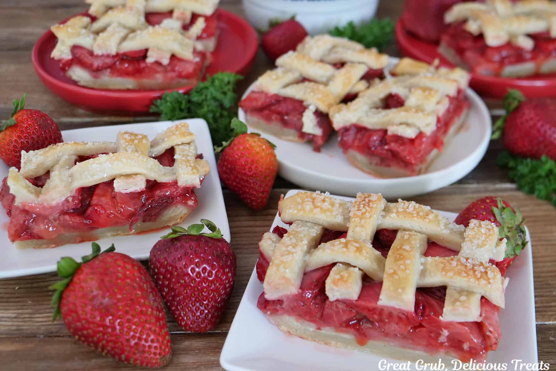 Strawberry pie bars on white plates with fresh strawberries randomly placed around and a bowl filled with strawberries in the background.