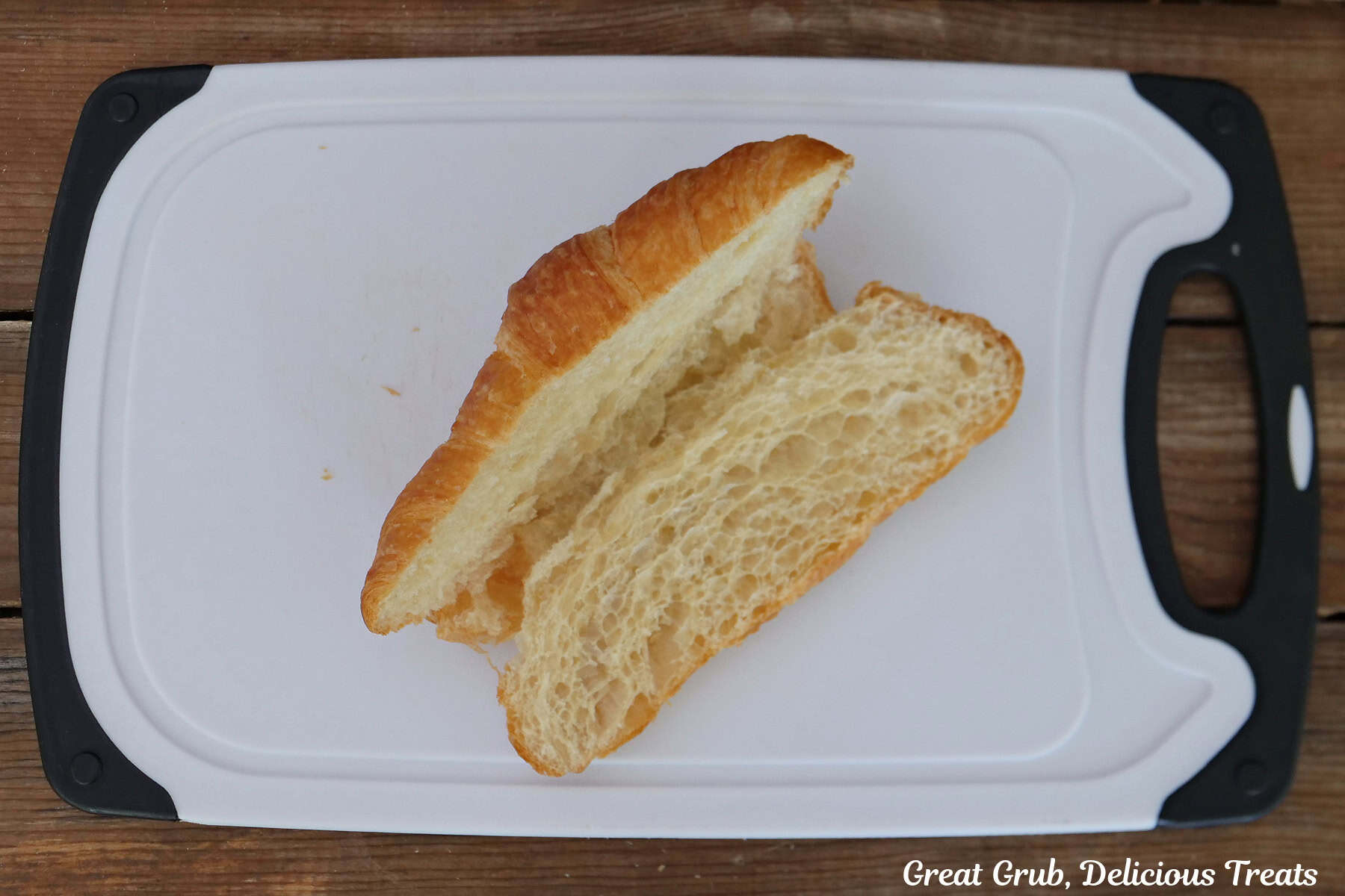 A white cutting board with a croissant cut in half on it.
