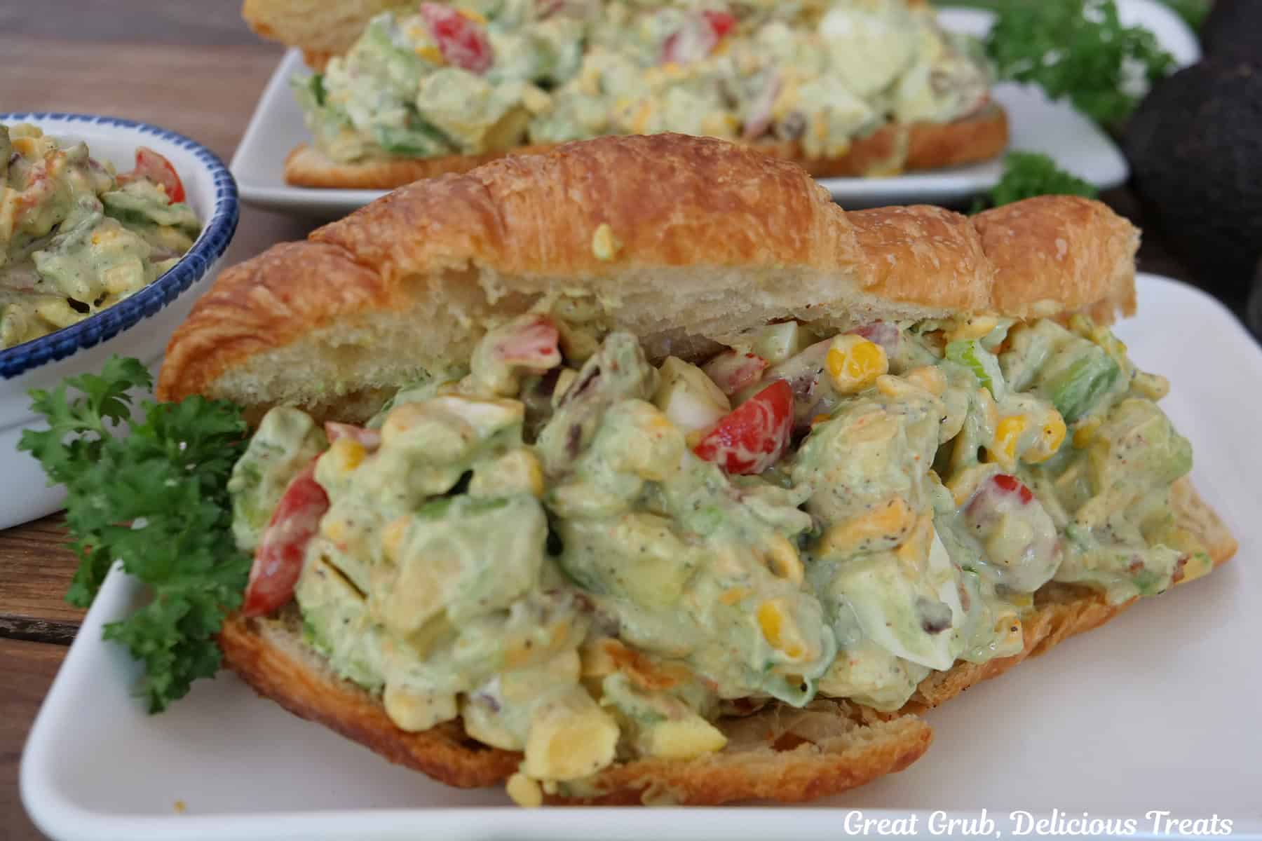 A white plate with a avocado salad croissant sandwich on it.