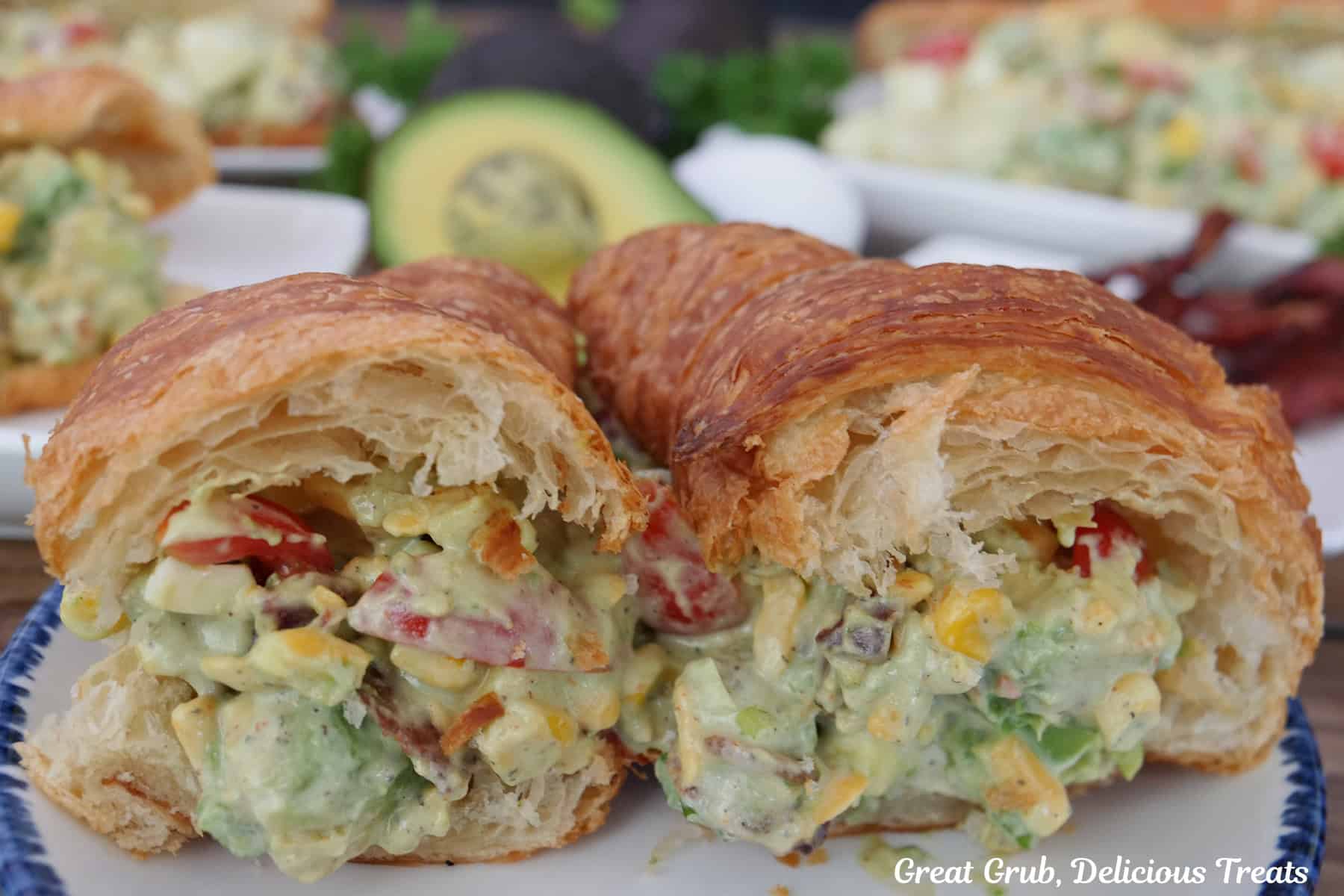 An avocado salad croissant sandwich but in half on a white plate.