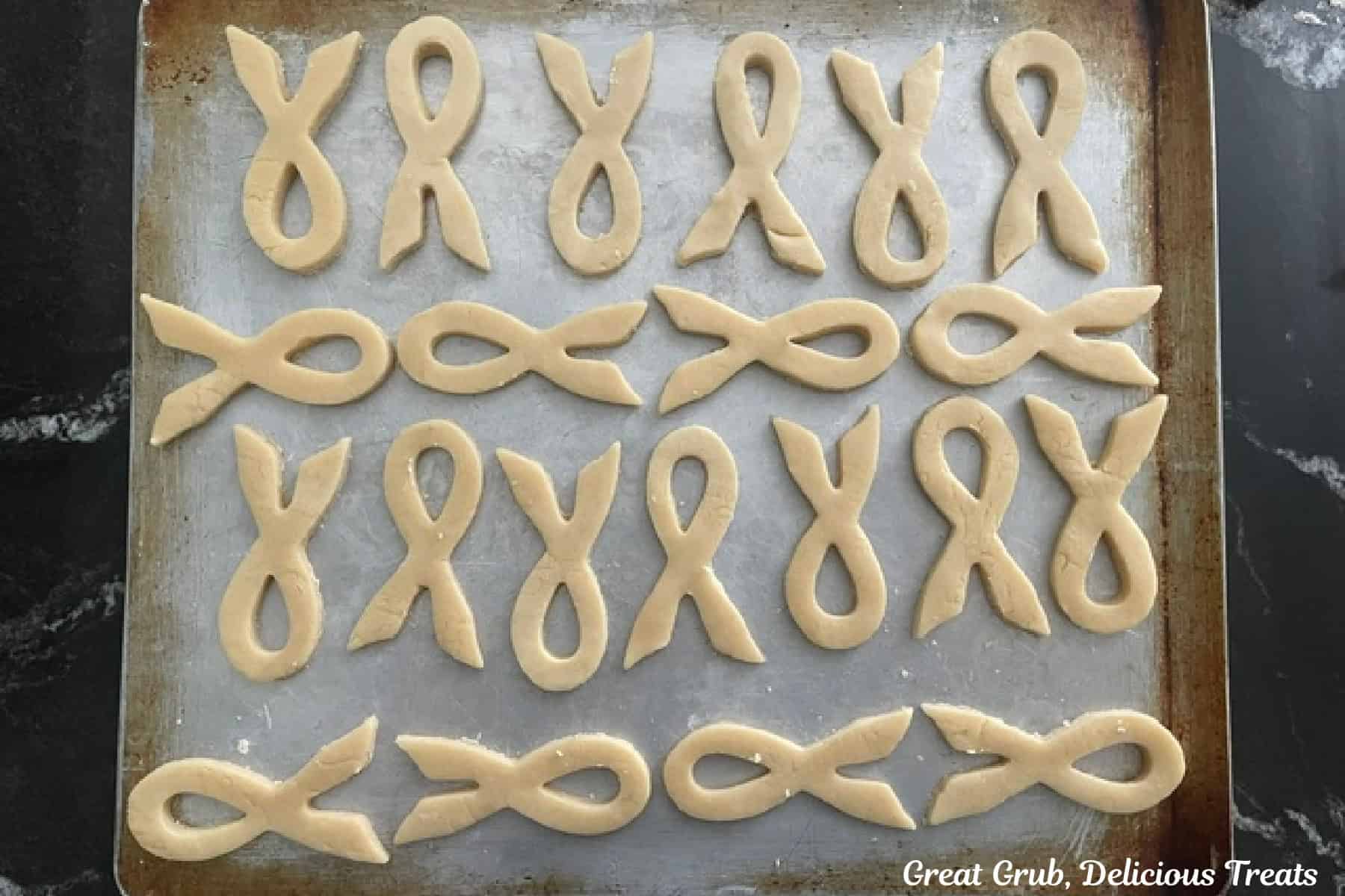 A sliver baking sheet with 21 ribbon cookies placed on it before going in the oven.