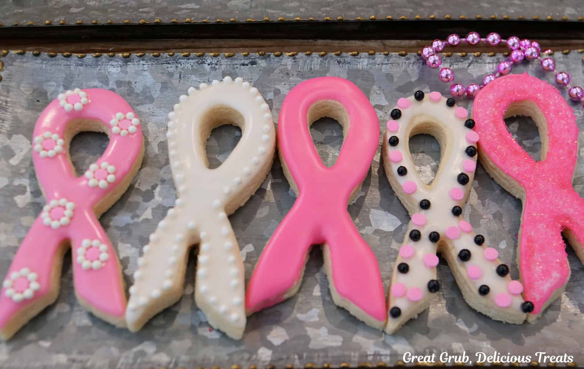 A silver tray with five breast cancer awareness ribbon sugar cookies on it decorated with royal icing in pink and white.